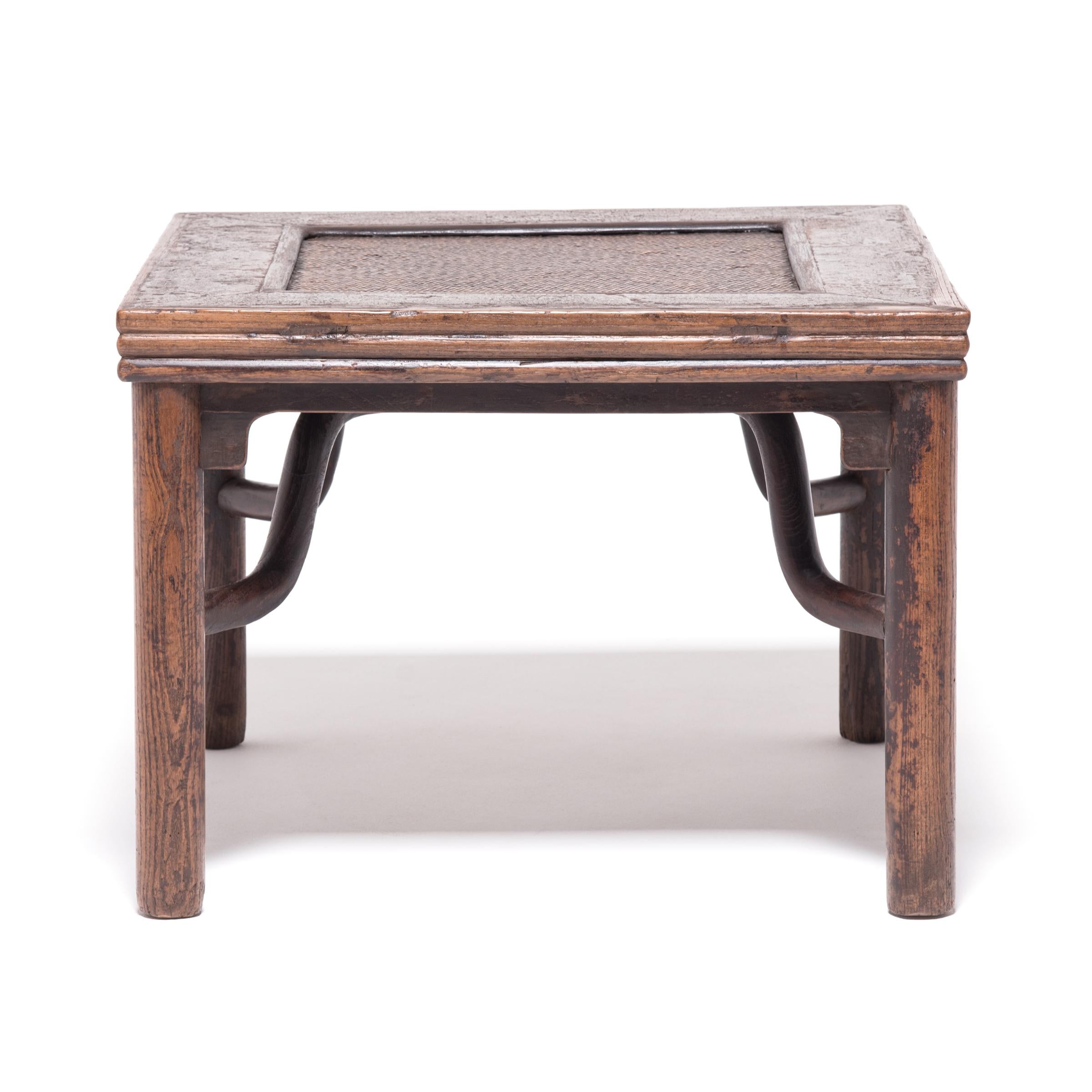 The fang deng, or square stool, form was popular for its simplicity and utility in the home. The simple legs, stacked edging, sinuous braces, and rattan top make this a particularly unique example. The timeworn finish combines with rattan and