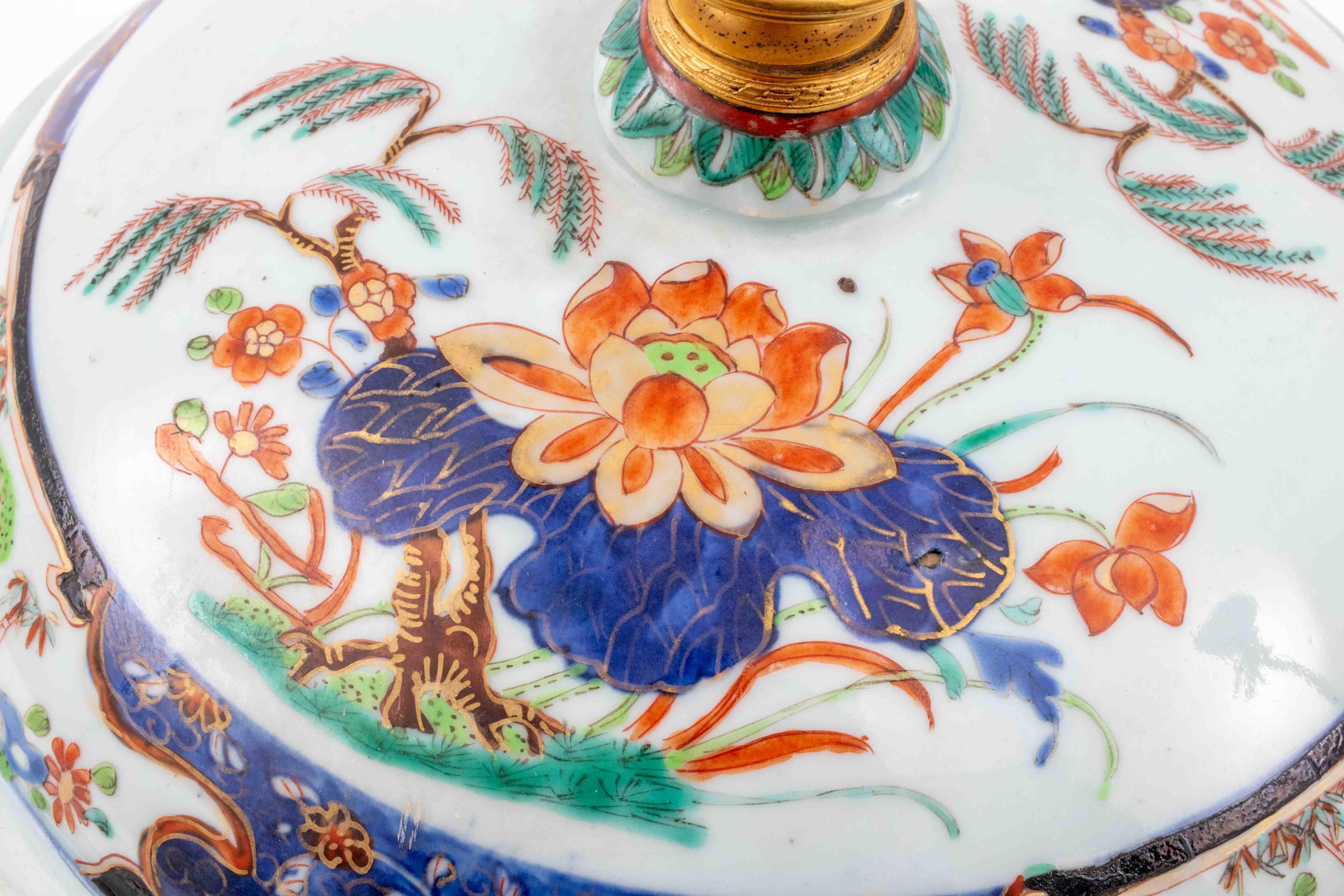 Chinese wucai porcelain jar with two figural animal handles in the shape of cat heads and hand-painted floral decoration with orchids, lotuses, and gold paint accents, topped by a gilt bronze finial encircled by a tobacco leaf border, previous