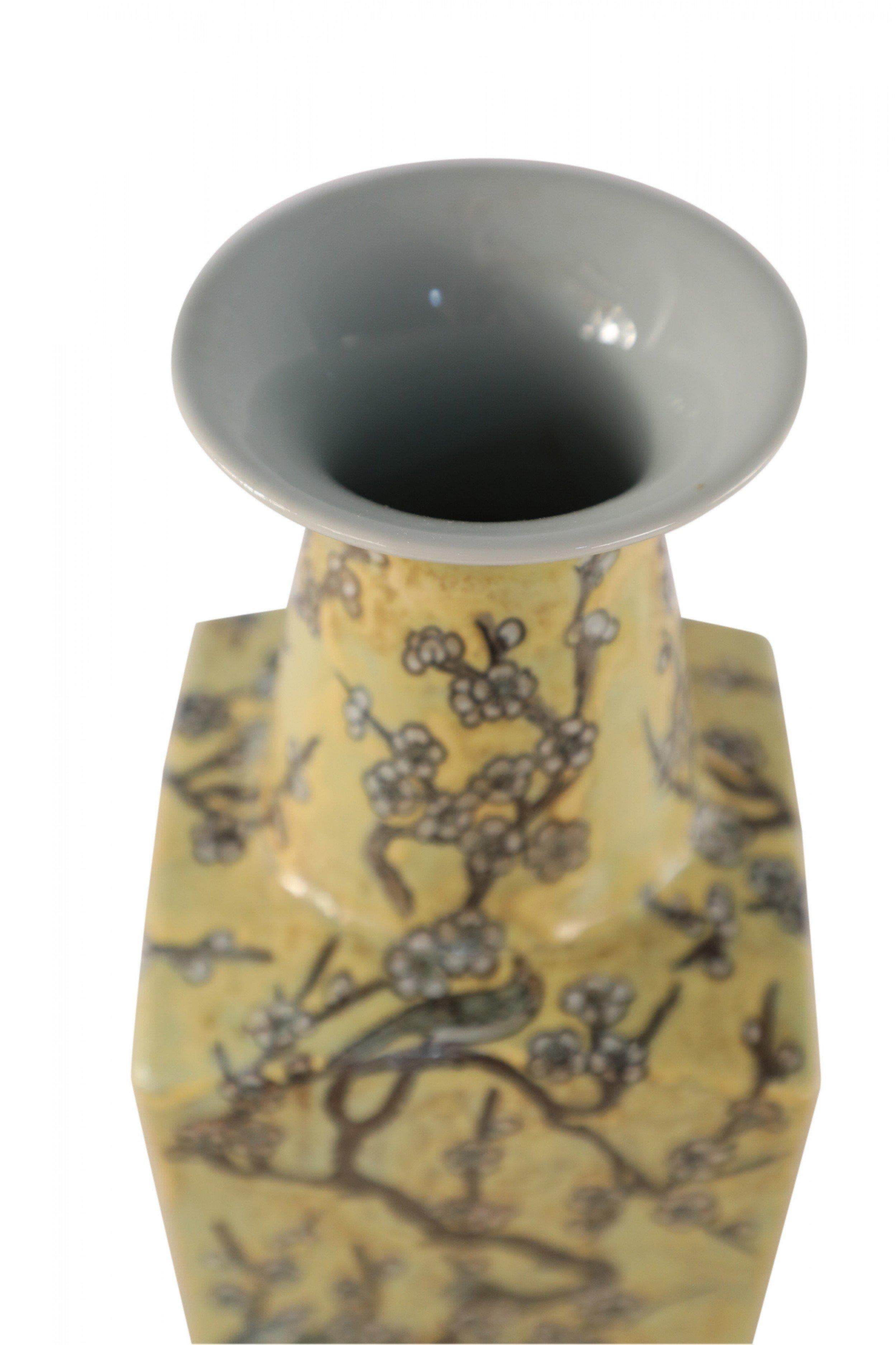 Vase à manche en porcelaine jaune de Chine avec des branches de fleurs de cerisier et des oiseaux dans une palette neutre pâle, enveloppant les quatre côtés et remontant le long du col.
 