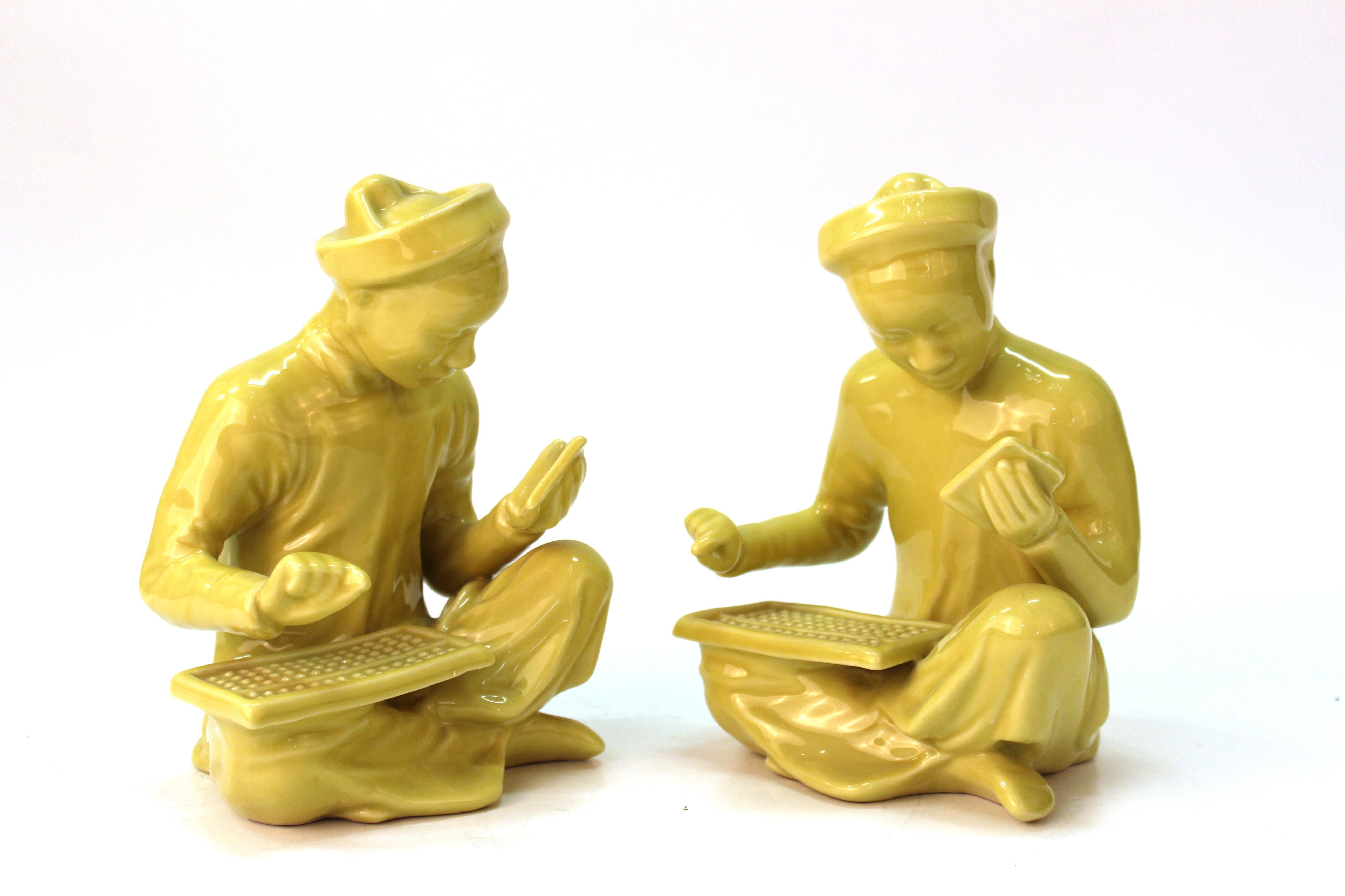 Chinese pair of seated mandarin statues in yellow glazed ceramic. The pair is in a seated position, at work with an abacus and scribe utensils. In good vintage condition with age-appropriate wear.
