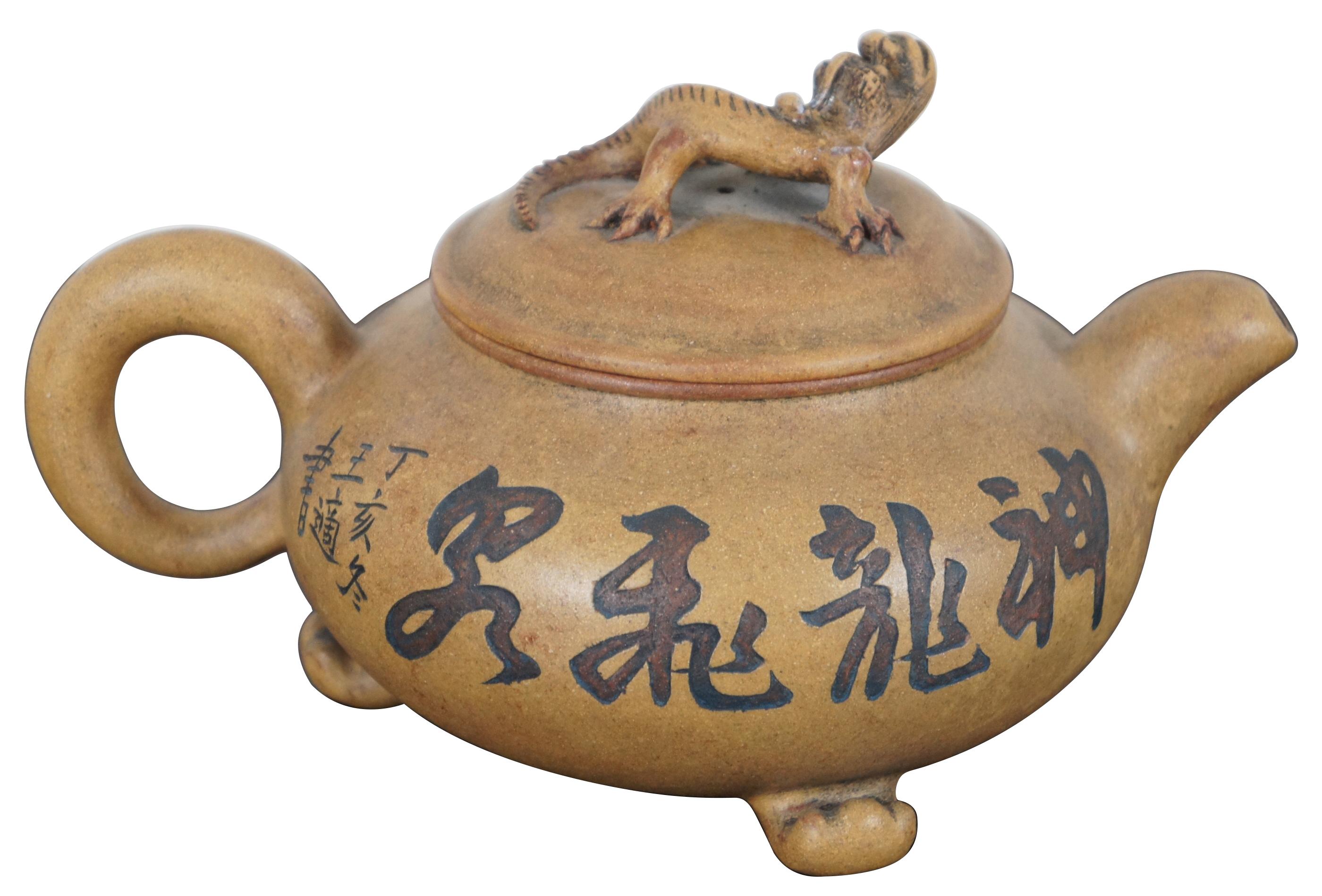 Vintage Chinese Yixing Zisha ceramic teapot with three feet, carved landscape and calligraphy on the sides and a lizard handle on the lid.
    
