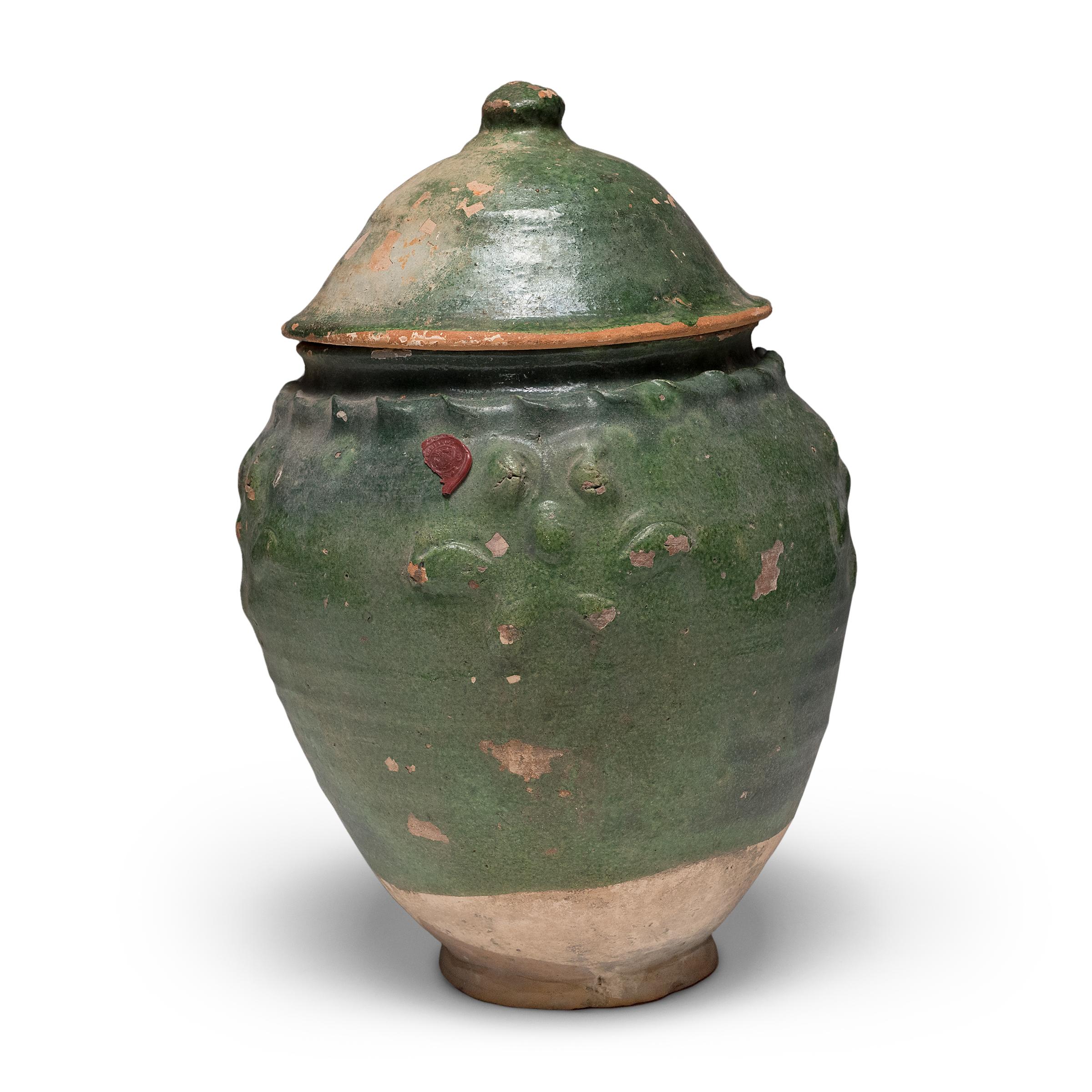 Belle dans son imperfection, cette jarre à couvercle émaillé vert de la province du Yunnan est un récipient à offrandes, ou jarre à esprits, qui contenait à l'origine des offrandes rituelles telles que des pièces de monnaie, des coquillages, des