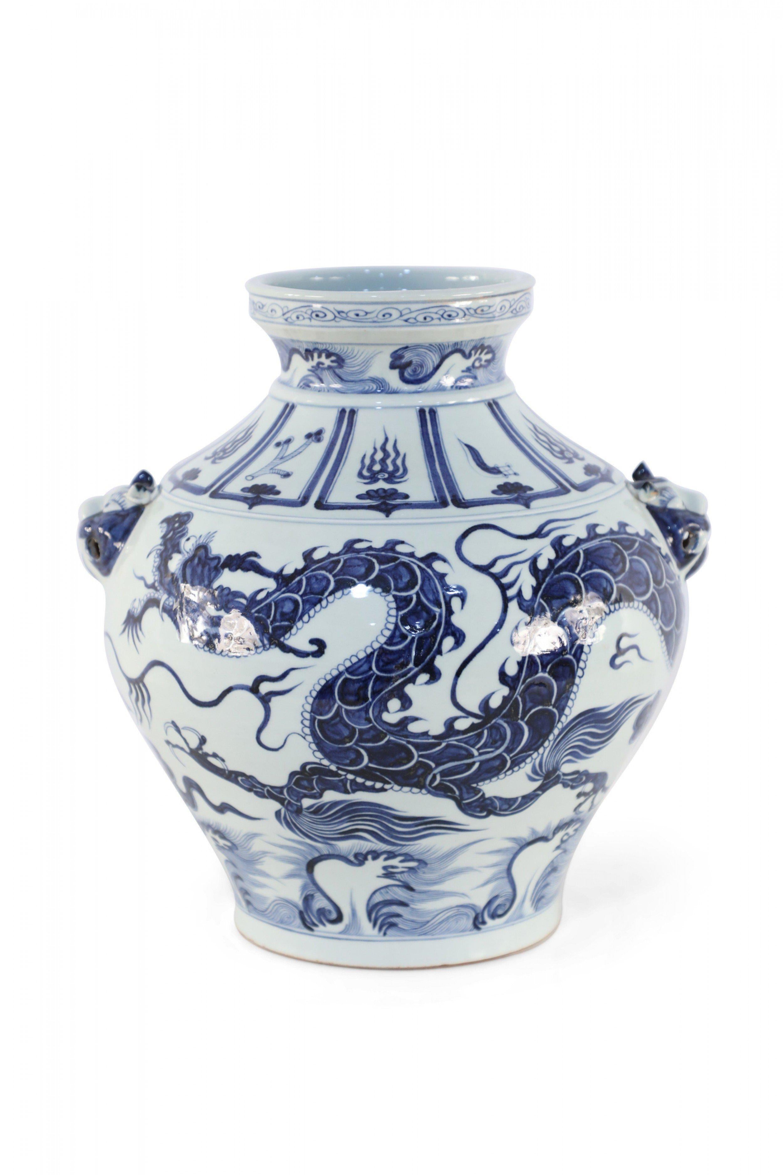 Chinese bulbous, white porcelain pot crafted in the Yuan Dynasty style, wrapped in a large scaled blue dragon on the body and decorative symbols around the neck, and accented with foo dog doorknocker ornamentation along the sides.
 