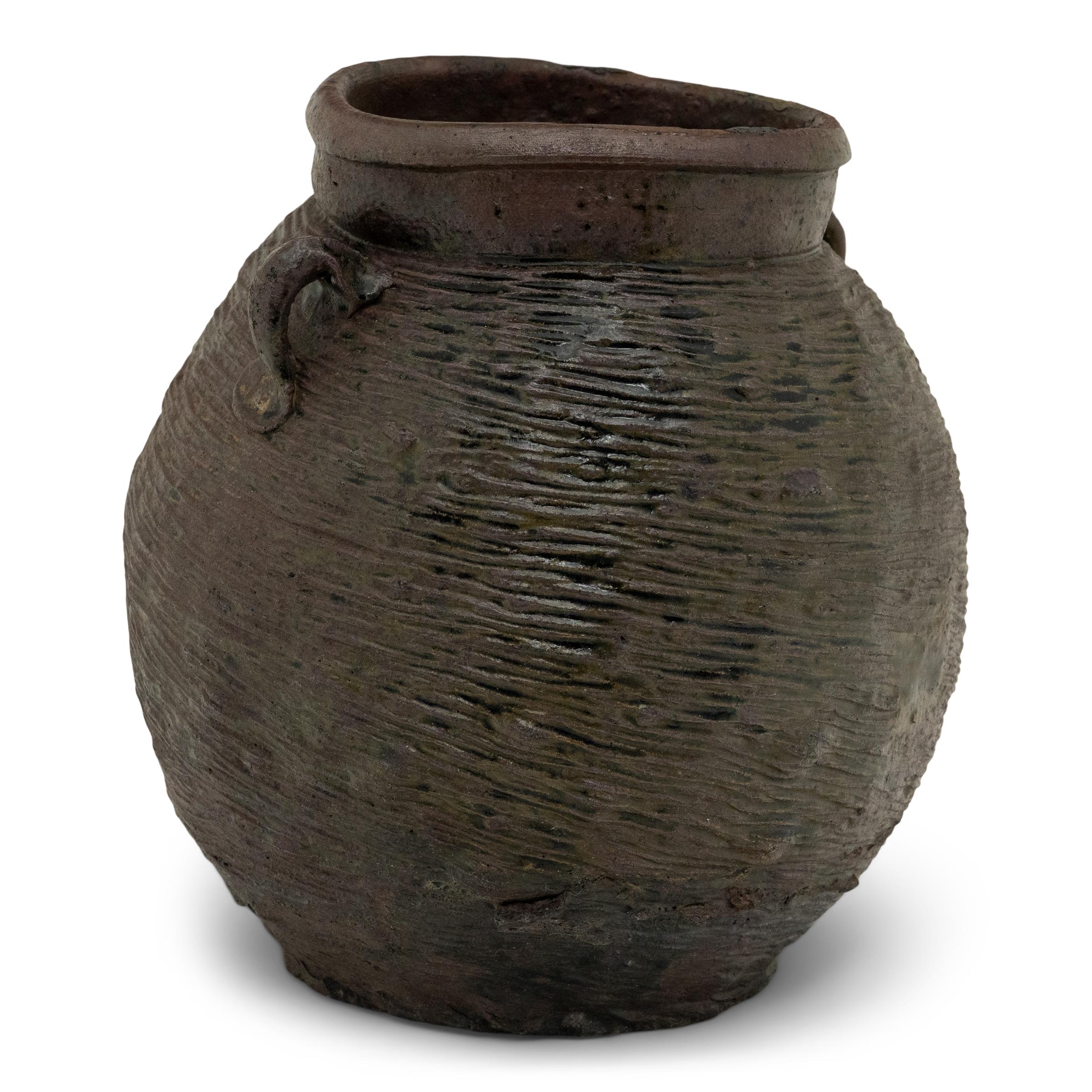 Dieser Steinguttopf aus dem 19. Jahrhundert, der mit einer schön unregelmäßigen braunen Schlickeroberfläche überzogen ist, hatte die bescheidene Aufgabe, in einer Küche der Qing-Dynastie trockene Waren zu lagern. Der gelappte Topf hat eine runde