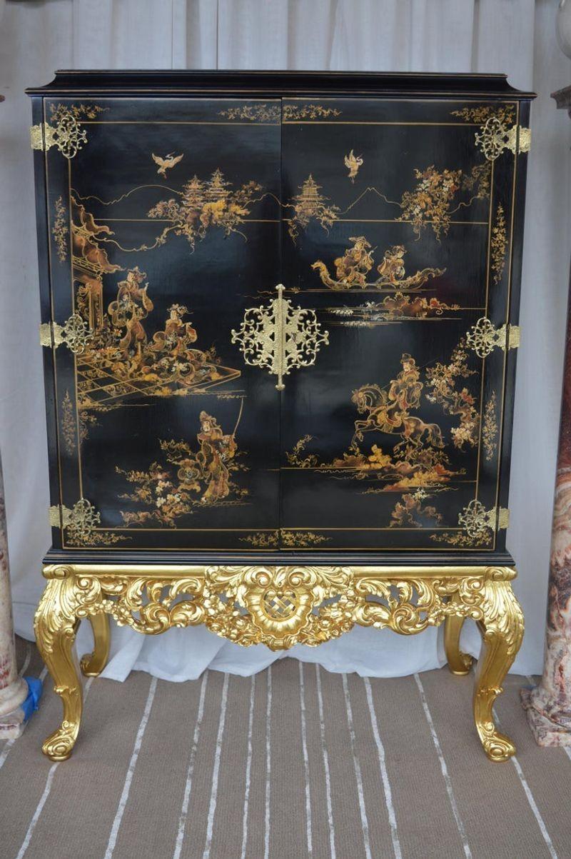Chinoiserie bar cabinet with a giltwood base. The bar cabinet has two glass shelves. It is lit from the top and the light turns off when the doors are shut.