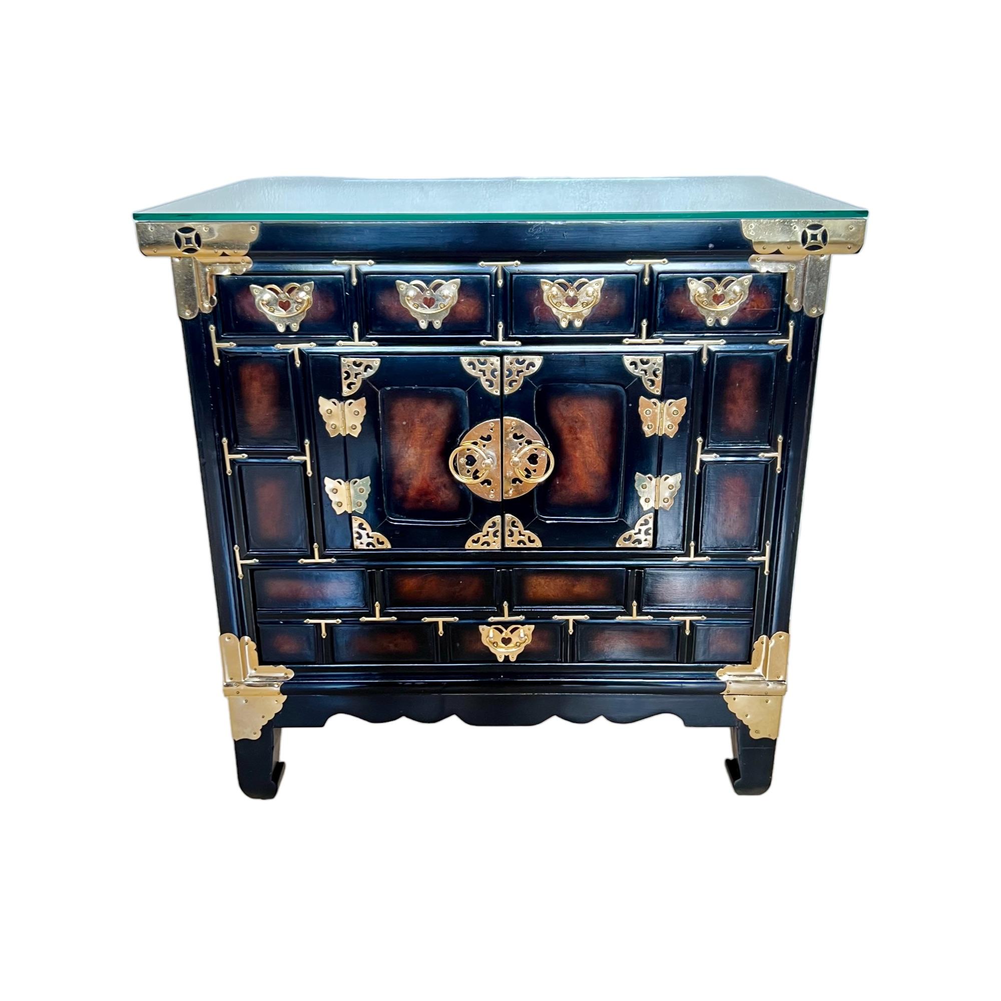 This vintage 1970's chinoiserie tansu style Asian nightstand or small storage chest cabinet is constructed of wood and has a Japanned black 'lacquer' finish with faux bois burl paneling on the top, sides, and drawer & door faces. It is raised on