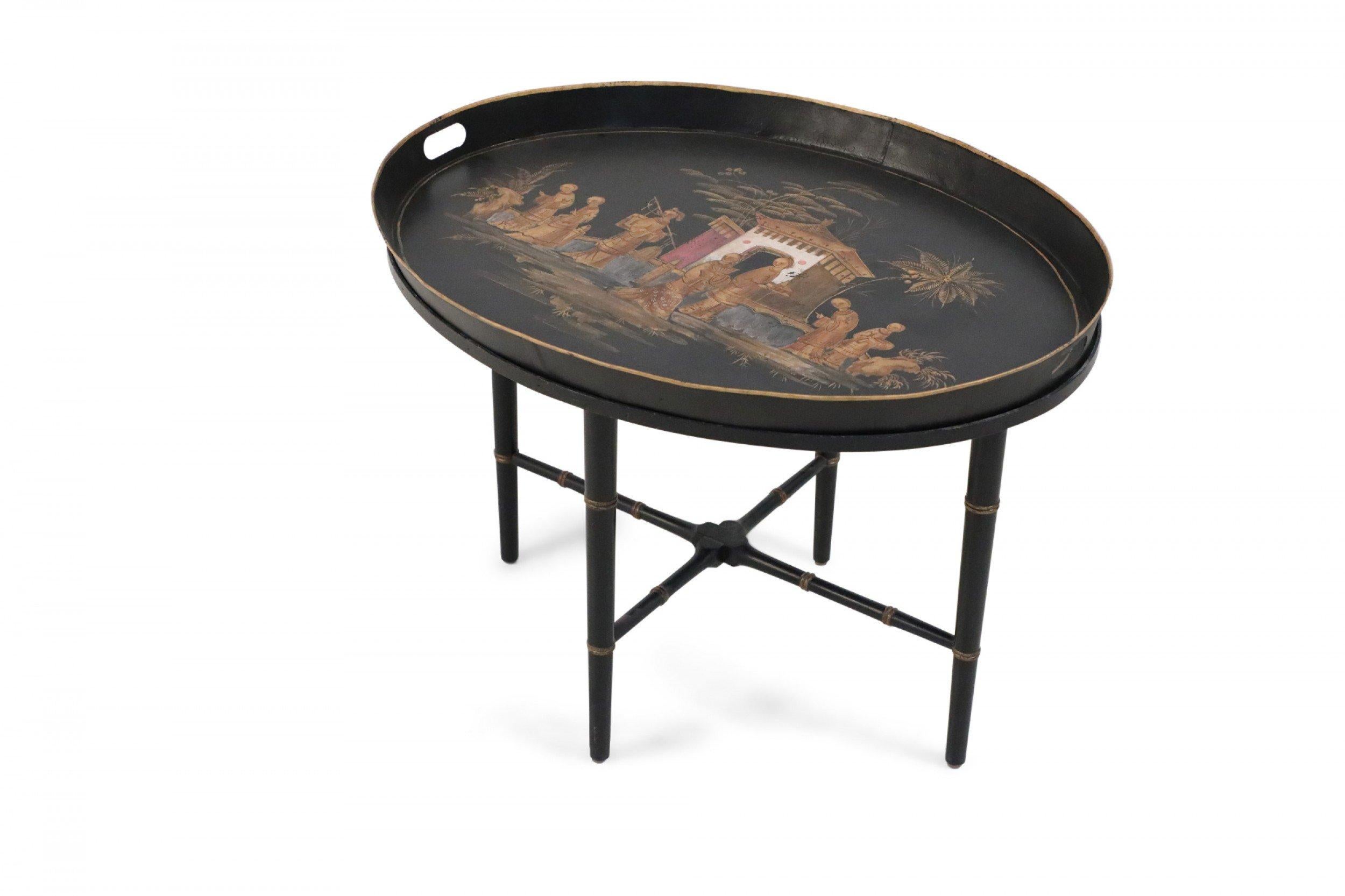 Chinoiserie tray top coffee table in black, topped with an oval, removable tray painted in a figurative scene, sitting atop ebonized faux bamboo legs accented in gold and connected with an x-shaped stretcher.
 