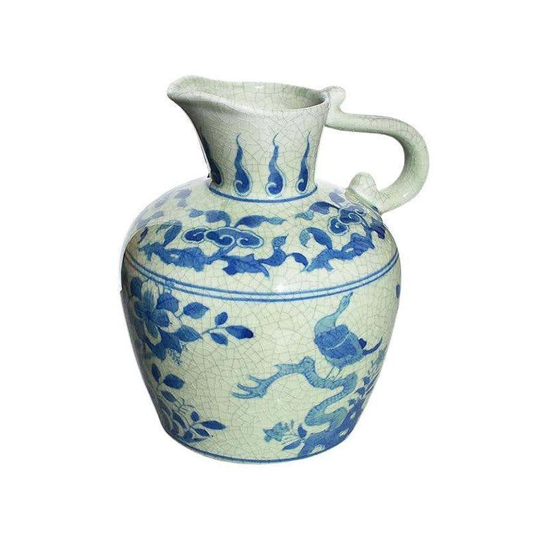 A beautiful chinoiserie ceramic pitcher in blue and white. This piece has a lovely craquelure finish. A floral design of birds and stylized flora and fauna are painted throughout in blue on a light blue background. The bottom is stamped in blue.
