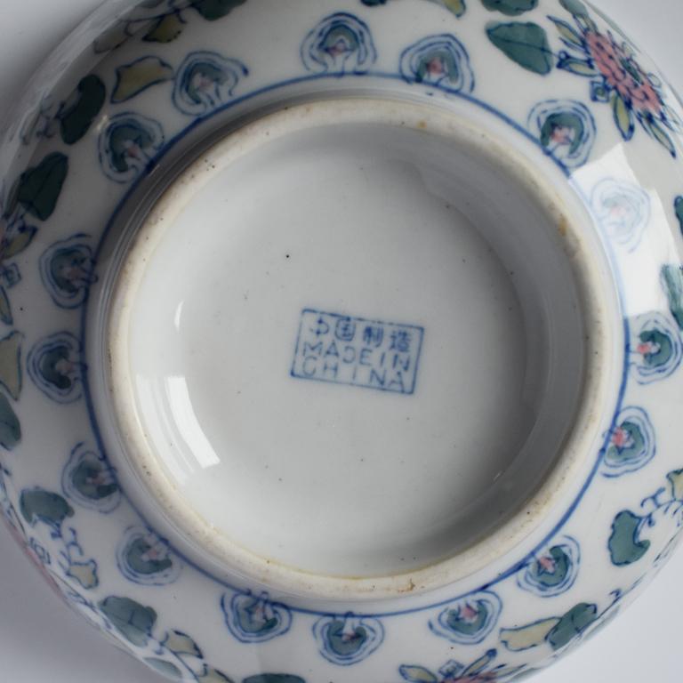 Round blue, white and pink chinoiserie bowl or serving dish. Around the outer edges, a blue line encircles the piece at the bottom and top. Throughout the center, scenes of pink geraniums and green vines adorn the piece throughout. 

The center of