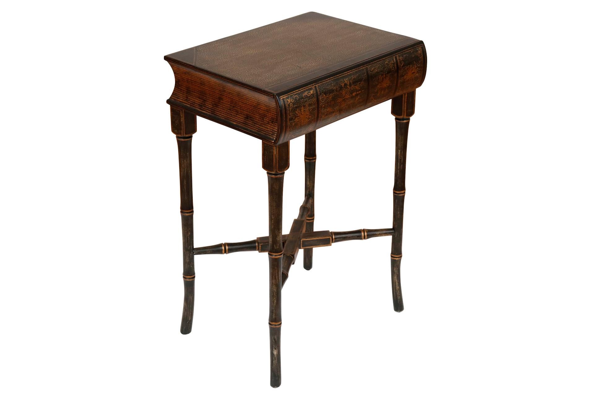A Chinoiserie side table with a faux book top made by Harden Furniture of NY. Faux bamboo saber legs connected with an x-stretcher support a table top carved to look like a thick book, the 'spine' of which opens to reveal a drawer. Lacquered black