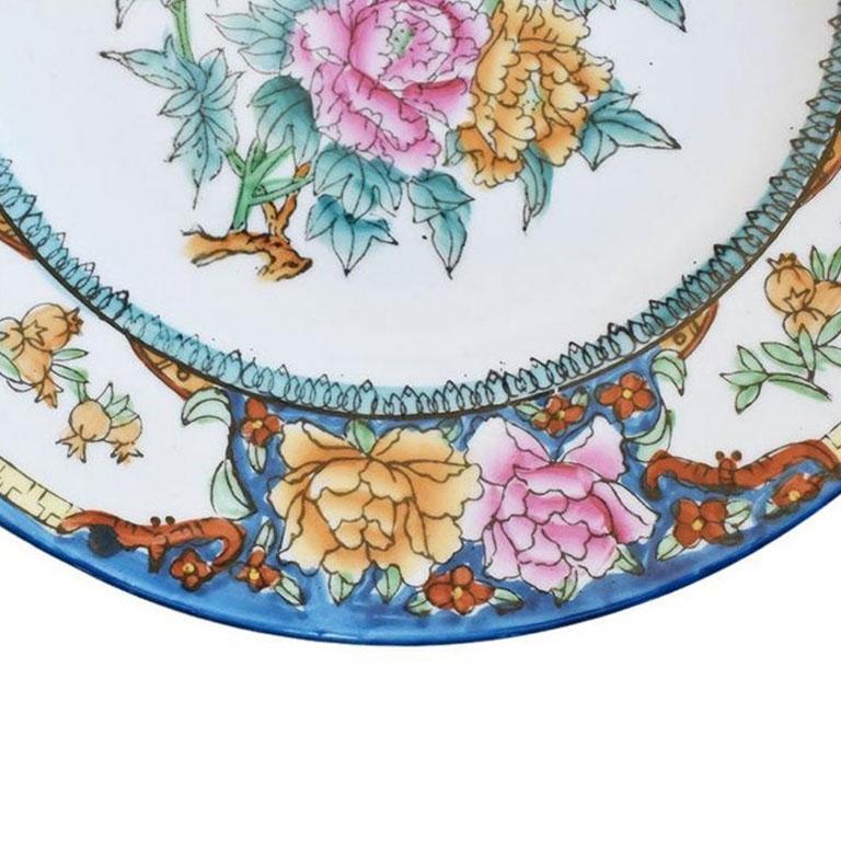 A small ceramic decorative chinoiserie plate. Decorated in a bright blue, this plate features chrysanthemums in yellow, red, and pink among lush green leaves. A hanger has been applied to the back to make hanging easy. We'd love to see this piece