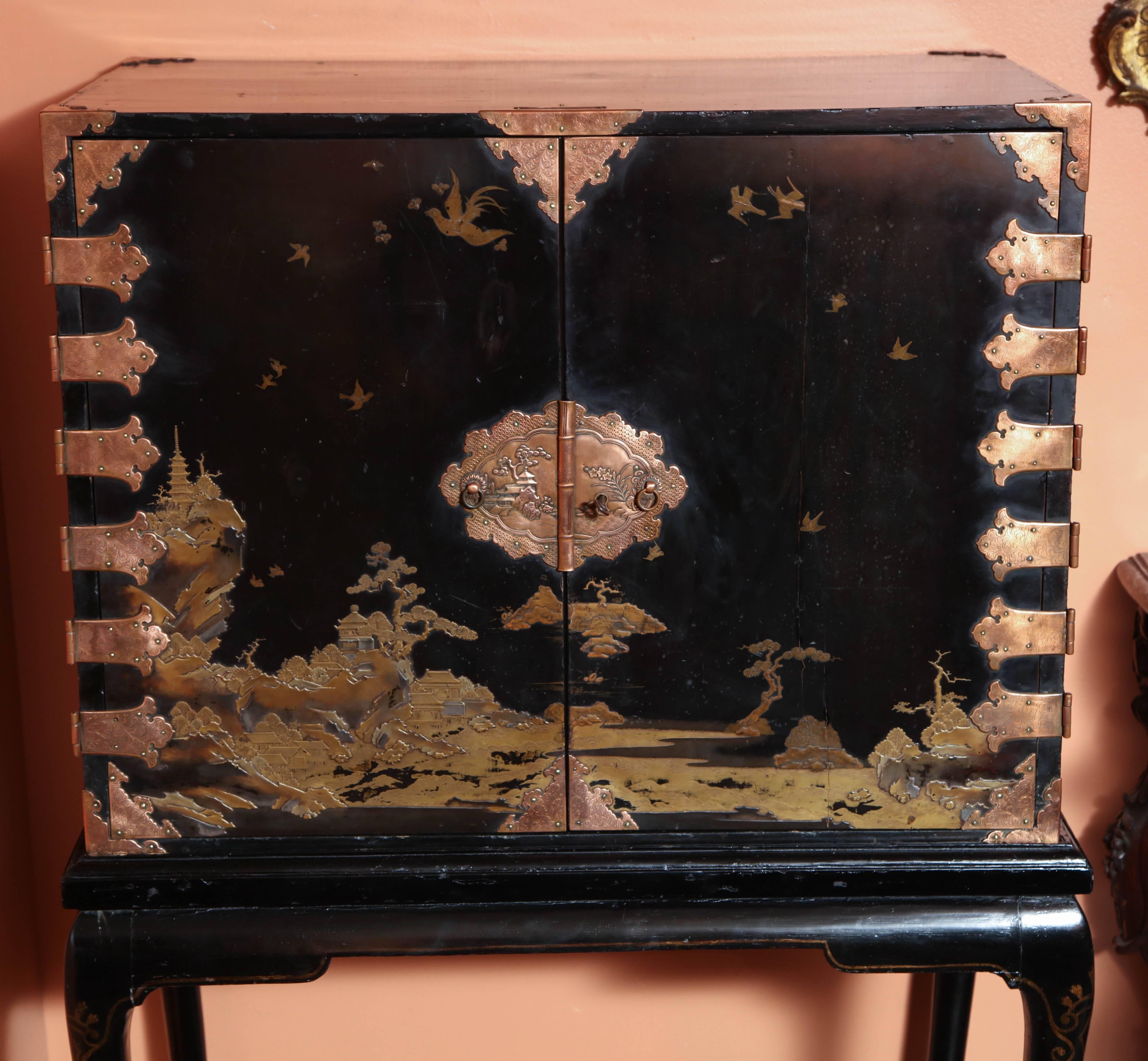 A Chinese export black lacquered Chinsoierie decorated cabinet with brass hinges and pulls raised and a Georgian style black lacquered base. The base is original and is decoratef with stenciling.