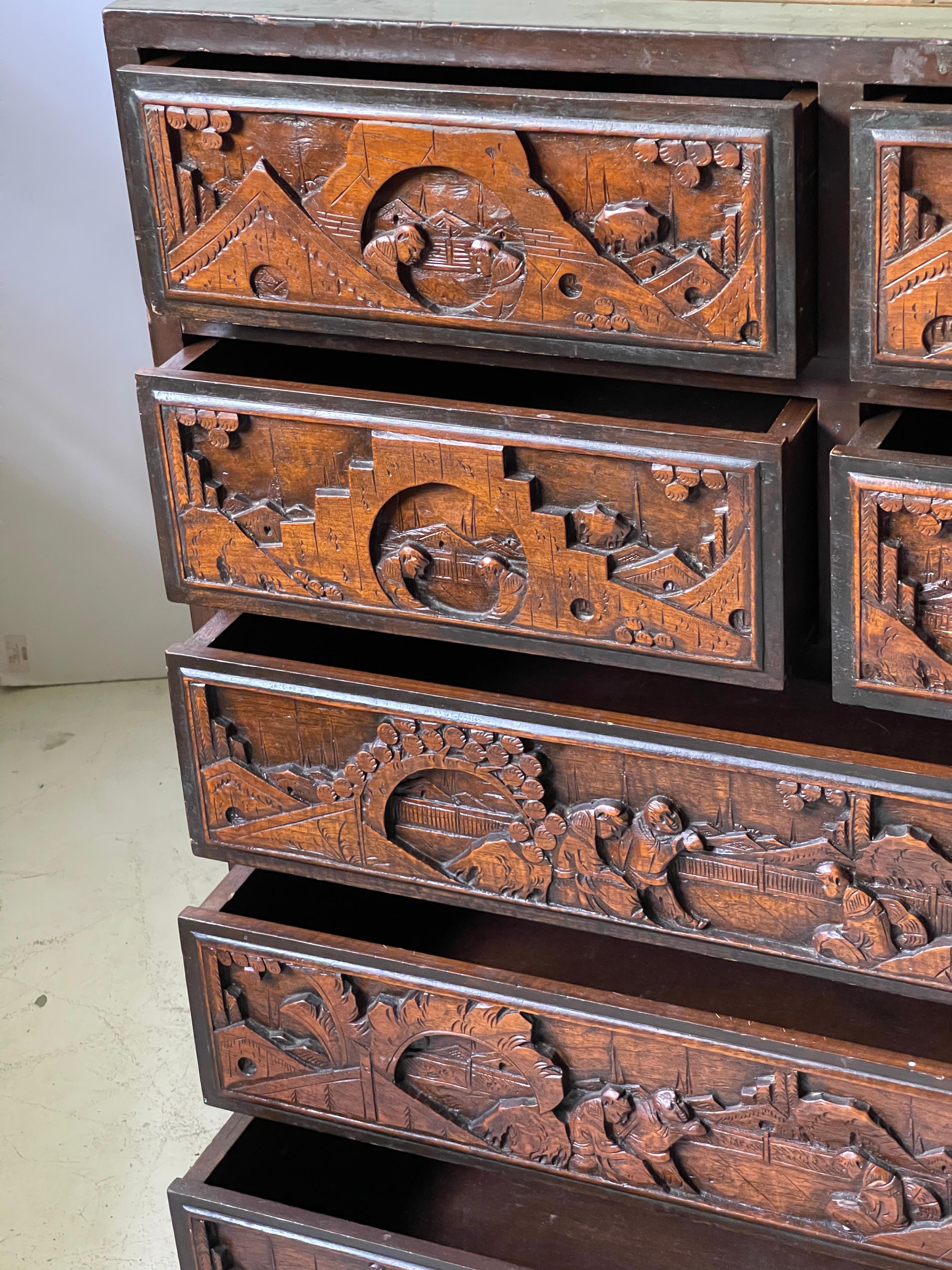 Early 20th century Chinese camphor wood figural carved batchelor's chest. This solid wood seven drawer chest features remarkable relief carved illustrations of wisemen in palace and garden scenes. Inset chinoiserie panels decorate the top, front,