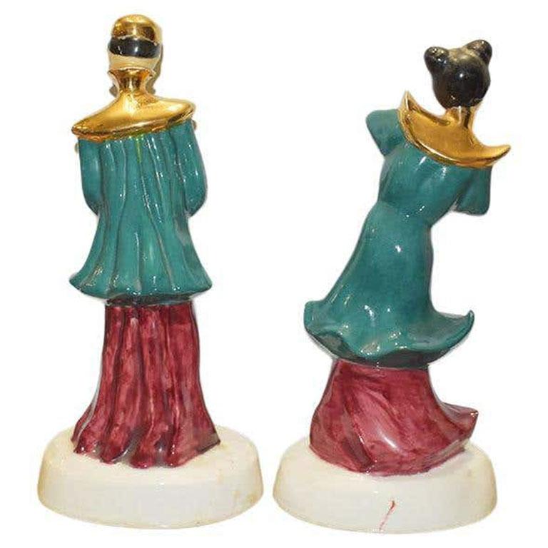 A pair of mid-century ceramic chinoiserie statues of a man and a woman in traditional attire. Both figures wear wonderful peacock blue-green tops with red bottoms. The man wears a gold head covering and the woman wears her hair in two buns. Both