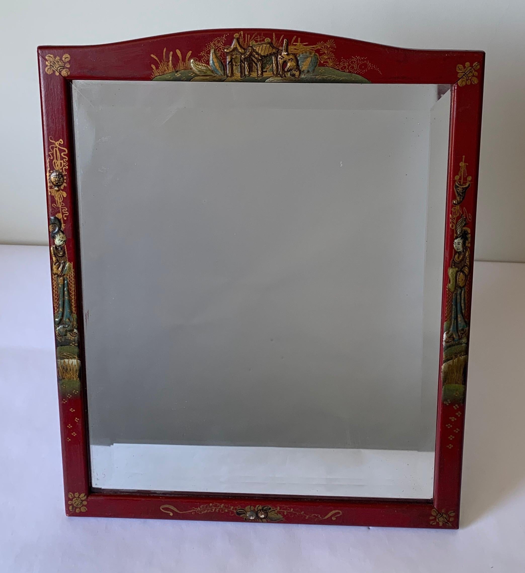 Cinnabar red chinoiserie vanity mirror with all-over hand painted gold chinoiserie detailing. Original bevelled mirrored inset glass. Original backing with easel stand and attached chain for hanging.