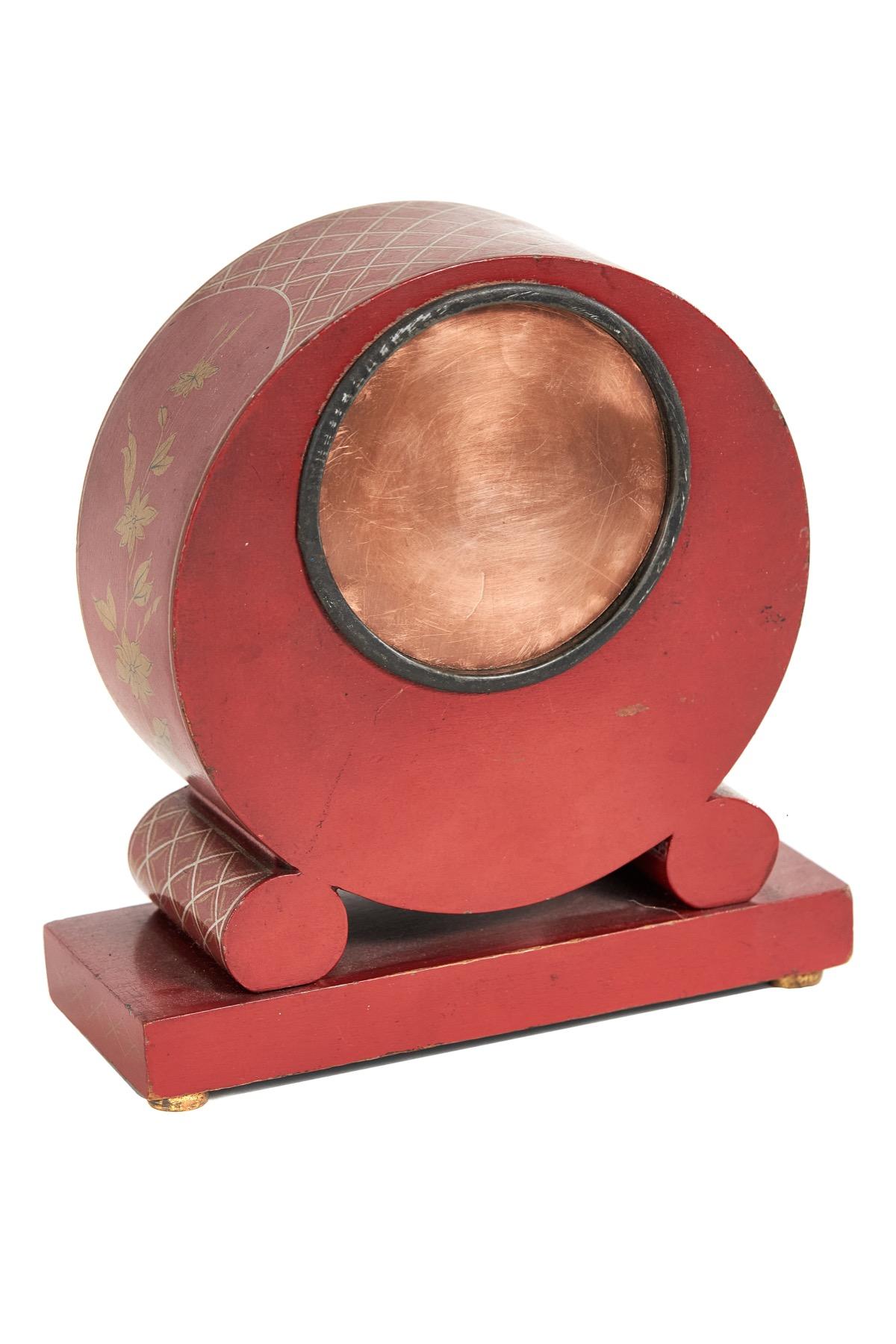 Chinoiserie-Kaminuhr, dekoriert, ca. 1930er Jahre
Die Farbe ist Rot und Gold, 
Kreisförmiges Gehäuse  gestützt durch zwei runde Bolster
Rechteckiger Sockel, 4 Messingfüße
Gehäuse mit Chinoiserie-Details verziert 
Kuppelglas, Oberfläche cremefarben