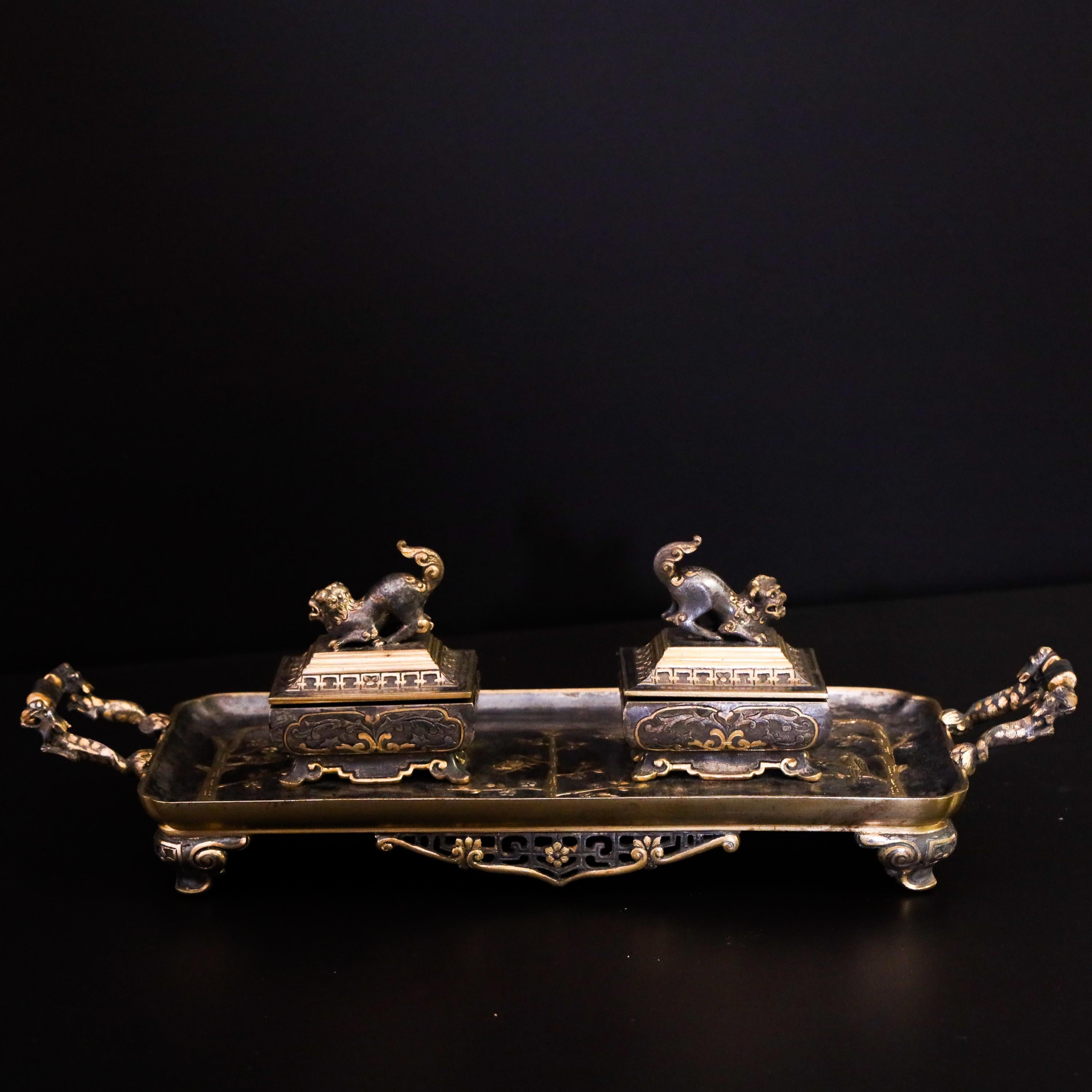 Chinese style metal desk set with side handles and two hinged chests with porcelain inserts. These are crowned by Chinese guardian lions. The tray is decorated with floral decoration accented in brass.
  