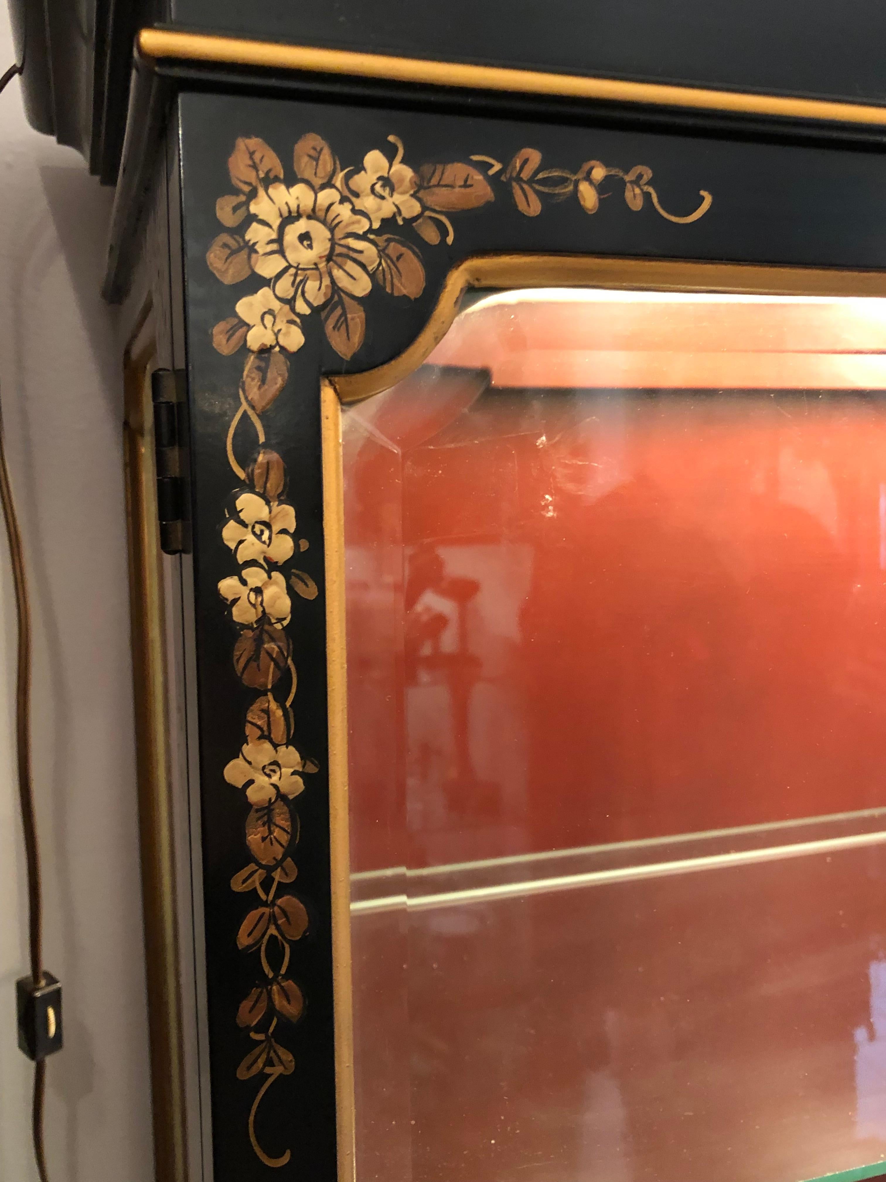A midcentury chinoiserie display cabinet with beveled glass on both sides and doors. Black case with gold accents and red interior. Lit from the top with four glass shelves, 2 of which have notches to hold plates. Pagoda style top 

