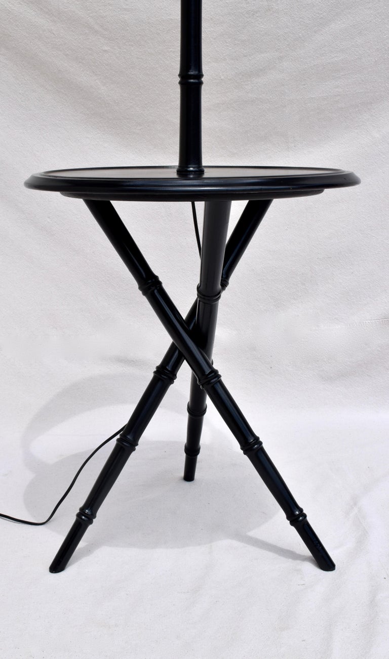 A mid-20th century black lacquered faux bamboo table with lamp, the upright stem & lamp being supported upon tripod base with Chinoiserie design characteristics. Includes the lamps original silk drum shade showing some signs of wear to the interior