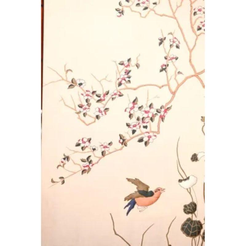 A vintage chinoiserie quilted fabric panel framed in faux bamboo.  The serene framed quilted fabric features a large branch with budding green leaves, white and red flowers and hovering birds set on a cream background
