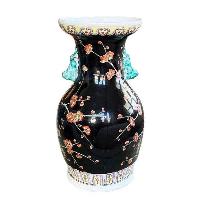 A tall famille noire chinoiserie vase with a red and green floral motif throughout the body on a black background. Attached to the neck of the vessel, are two green dragon or lion handles. The base of the vase has a pink, yellow and blue stylized