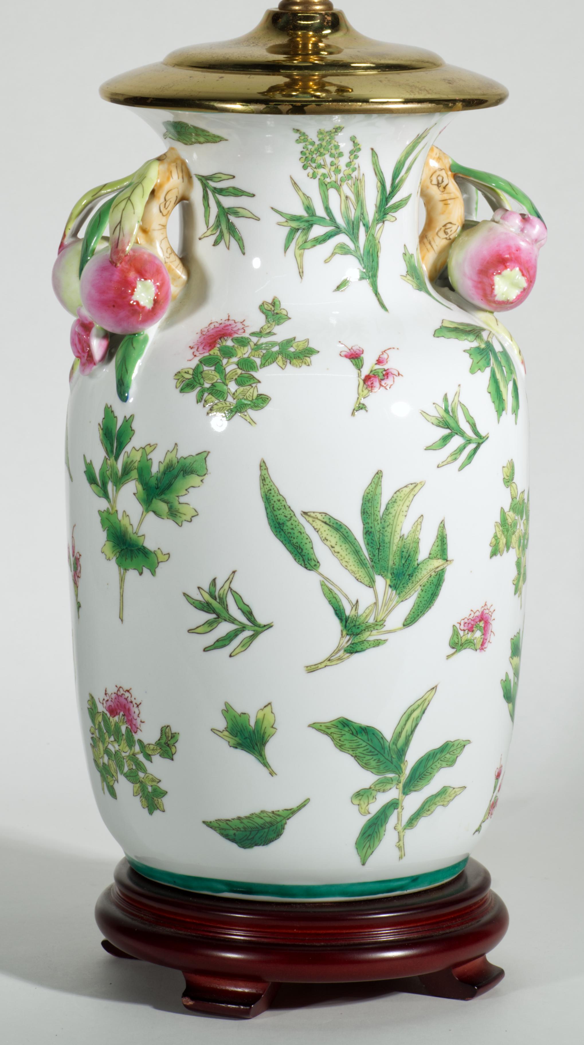Vintage Chinese Export table lamp features Famille Verte Rose decor on ceramic ginger jar body with double pomegranate relief handles. The lamp is mounted on carved wooden base and fitted with brass fixtures and ornate finial. Detailed Chinoiserie