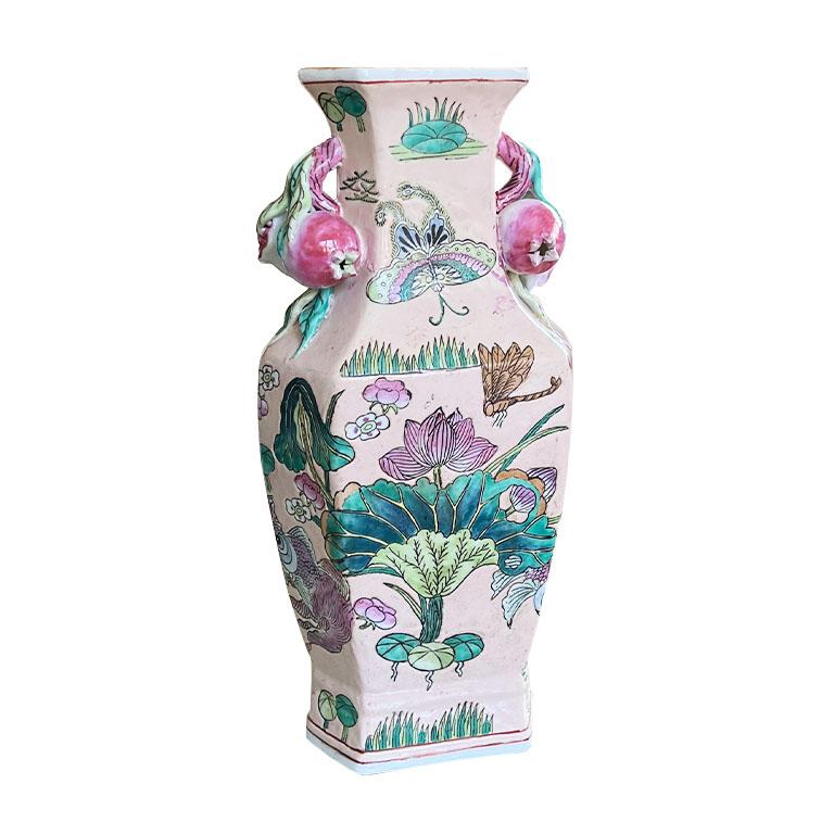 A tall ceramic chinoiserie famille rose pink vase with pomegranate relief handles. On a hexagonal base, this pretty pastel pink vase features hand-painted scenes of a pond. Ducks in pink, blue, and orange swim amongst green lotus flowers and lily