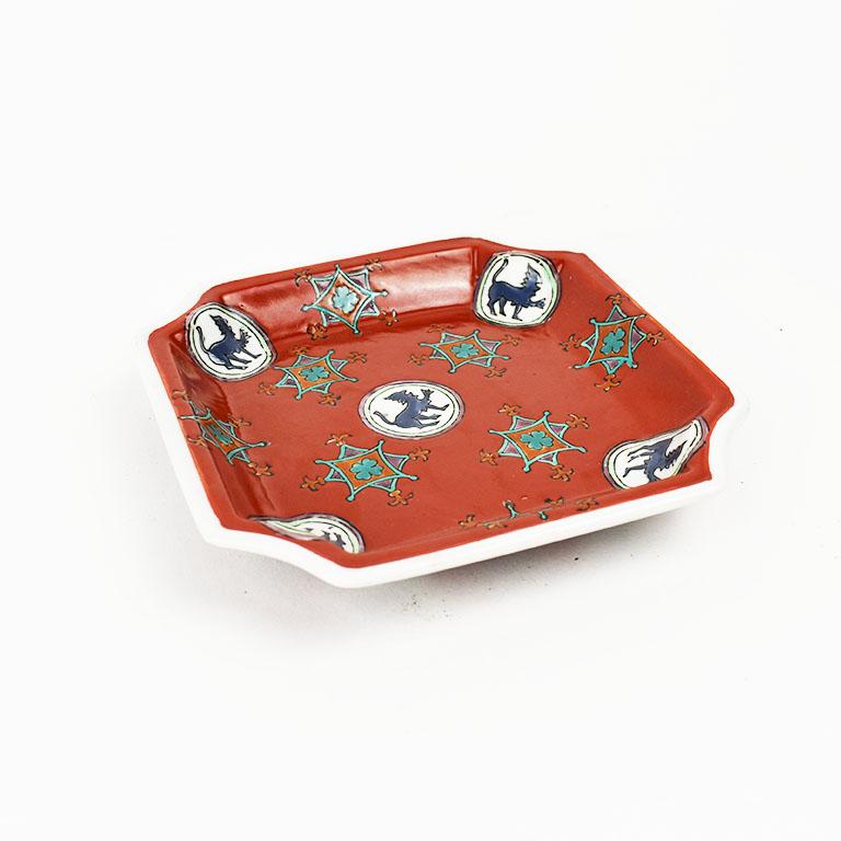 A lovely trinket dish or vide-poche decorated in a whimsical chinoiserie design. With four sides, the corners are scalloped creating a hexagonal shape. The inner portion of the dish is glazed in a vibrant red. Five blue foo dogs are encircled in a