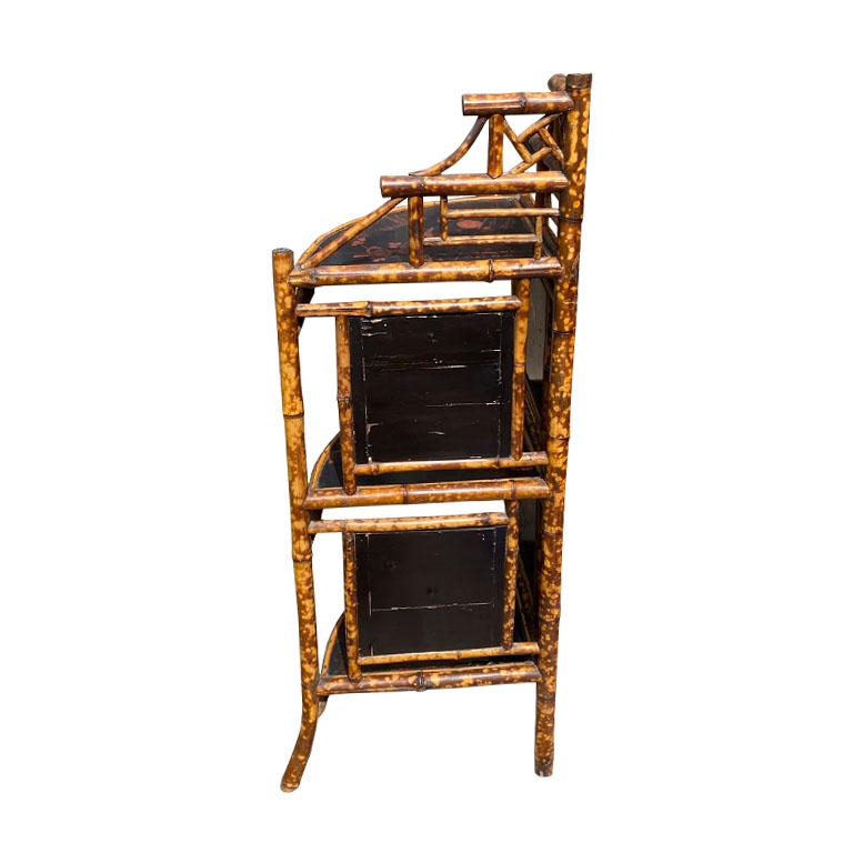 An antique English 3 tier corner etagere of burnt bamboo and black Japanned panels. Each shelf is fan-shaped and Japanned In black, with a red chinoiserie design of birds and flowers. 

The back of each shelf is flanked by the same ebonized black