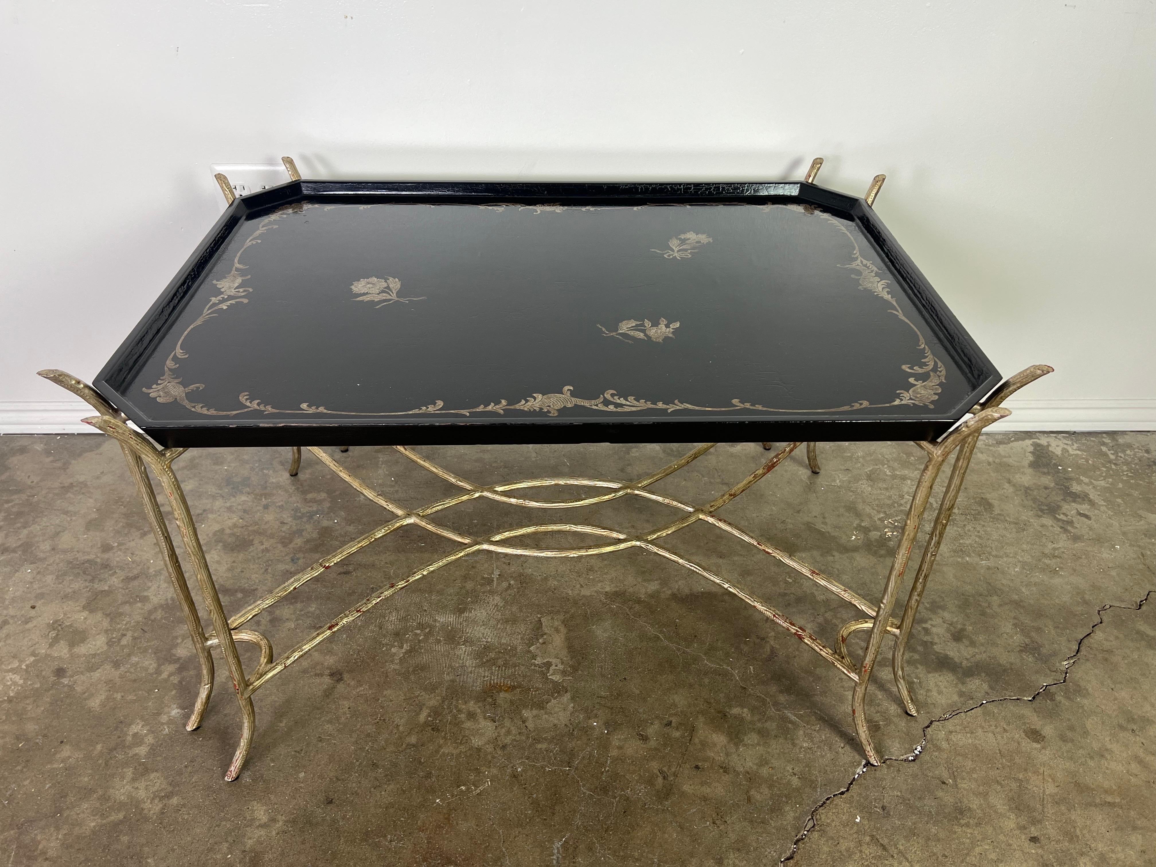 Black lacquered Chinoiserie painted tea table that stand on silvered metal legs that are connected by a bottom stretcher. There are are raised gold chinoiserie details of flowers and acanthus leaves. Good condition.
