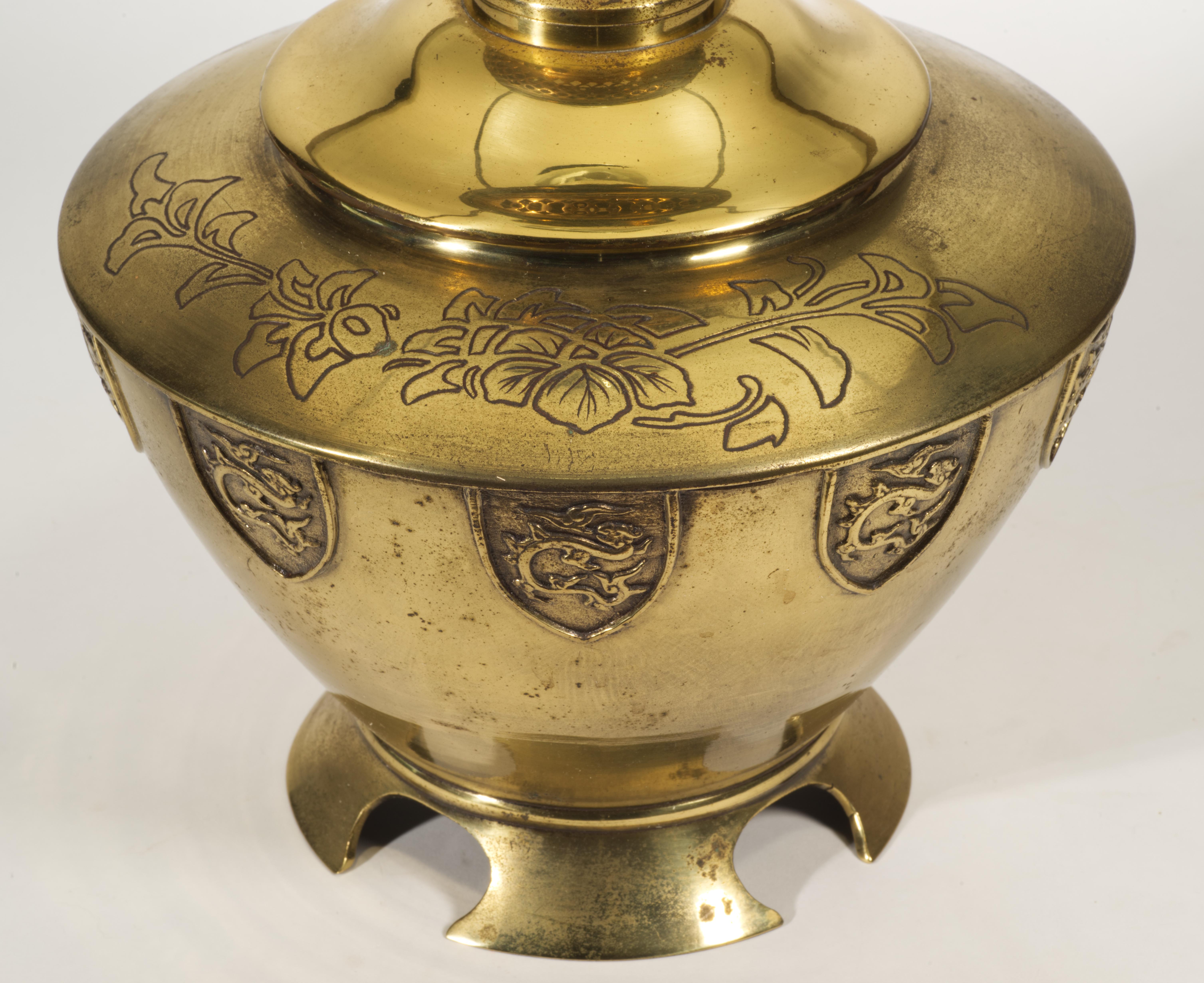 Antique or vintage large bronze lamp features striking Chinoiserie style urn body with a band of textured coat of arms shaped motifs of flying Asian dragons on the widest part of the body. The bronze urn is decorated with asymmetrically placed