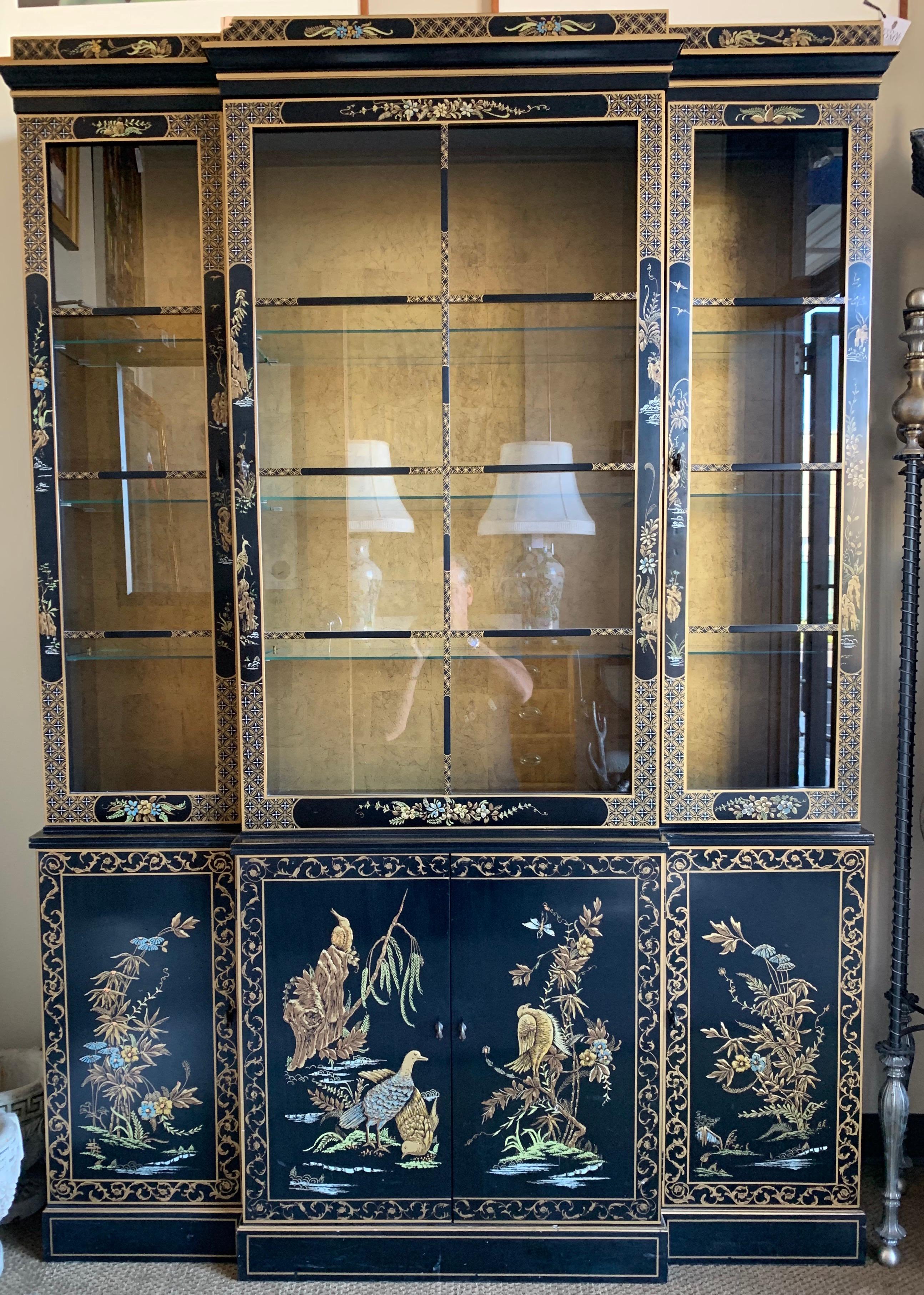 Elegant mid century chinoiserie japanned 2 piece china cabinet features beautiful hand painted motif of birds and flowers and gold detail on the front and sides. Two top front doors open to glass shelves which illuminate from above. Background is