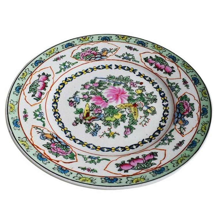 A small ceramic decorative chinoiserie plate. Decorated in a mint green around the edges, this plate features chrysanthemums and butterflies in yellow, red, and pink among lush green leaves. A hanger has been applied to the back to make hanging