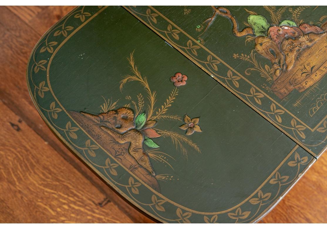 Chinoiserie paint decorated drop leaf table with raised enamel painting depicting a fisherman, scenic landscape, florals and gilt embellished. The leaves supported by wooden brackets and having a single drawer, gold paint decorated trestle form legs