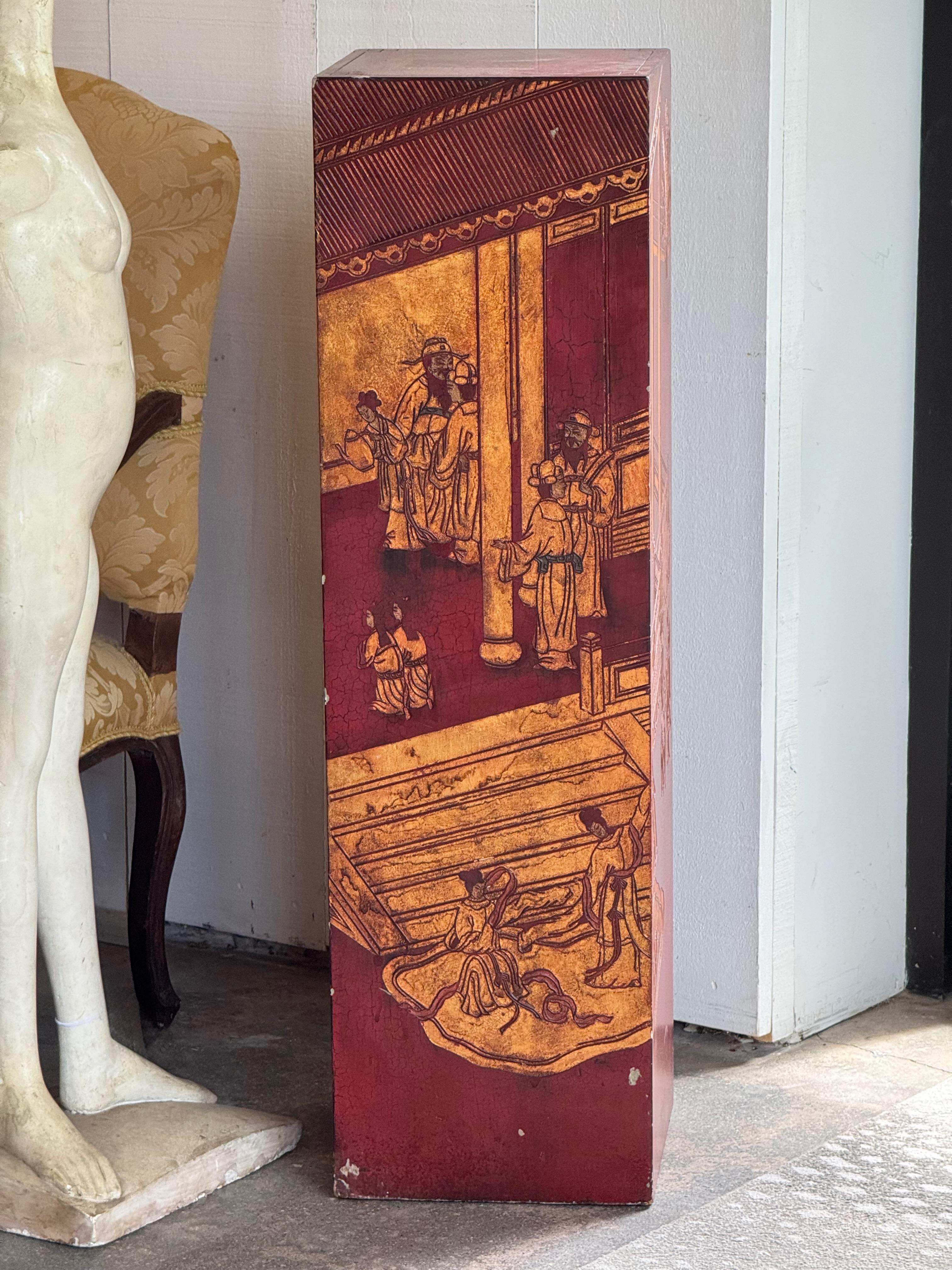 Tall rectangular pedestal in the chinoiserie style, finished in deep red lacquer with golden figural and architectural scenes on all sides. The surface shows intentional craquelure, adding texture and aged character. A decorative stand ideal for