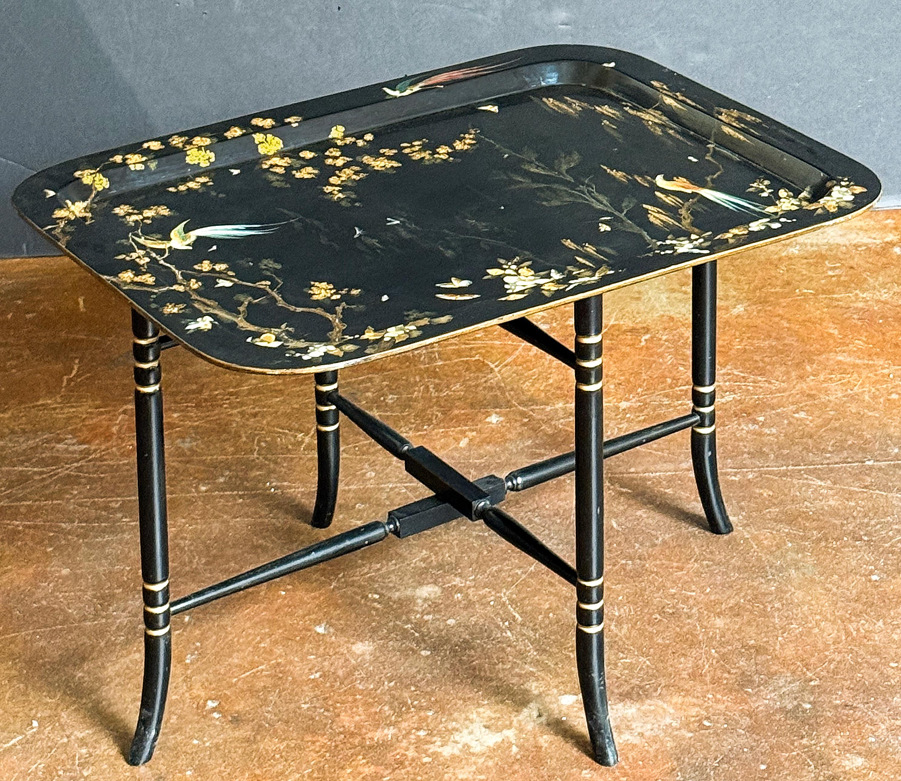 A beautiful English tray table or tray on stand from the Aesthetic Movement Period, featuring a rectangular tray of papier mache with a recessed center showing a decorative Chinoiserie painting of birds of paradise, with gilt trees and leaves. The