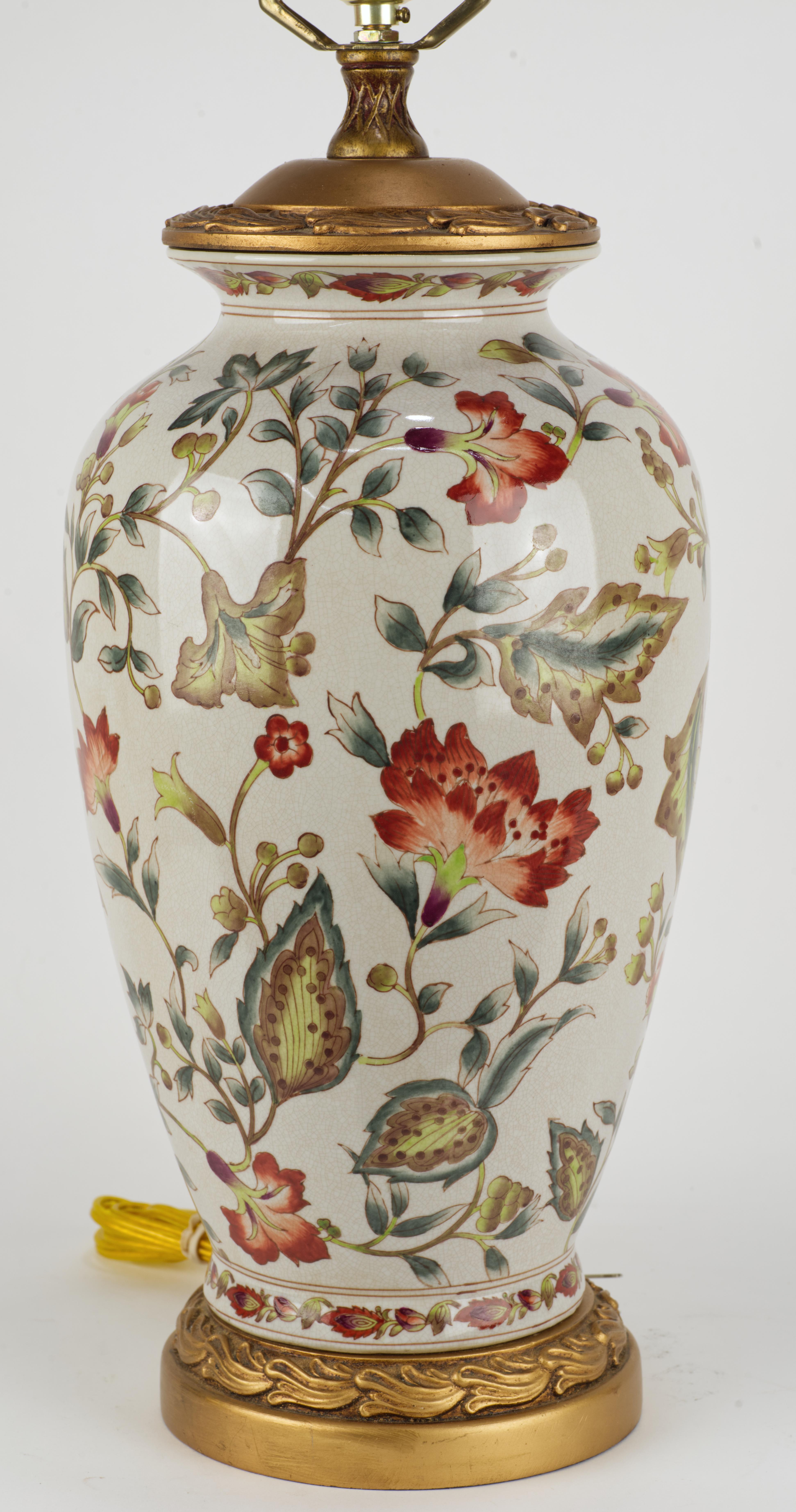  Die auffällige große Tischlampe ist mit traditionellen Motiven von Blättern und Blumen in blauer, roter, gelber und grüner Farbpalette auf einem leicht craquelierten, cremefarbenen Glasurgrund verziert. Der bronzefarbene Sockel und der Deckel sind