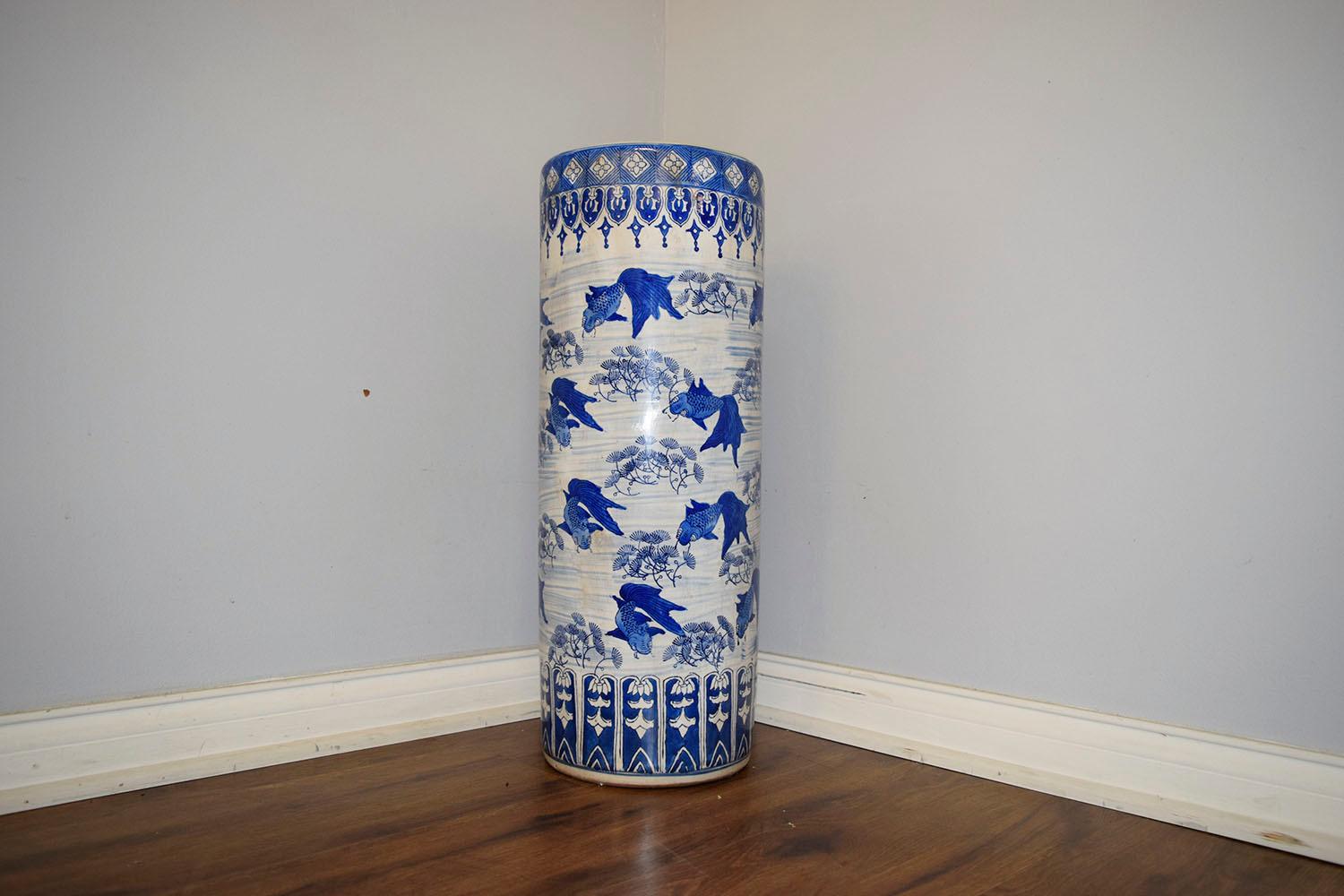 This 1950s Chinoiserie-style umbrella stand is made of porcelain with a white background and painted blue scenery. The umbrella stand depicts koi fish and sea plats all around, with unique design on top and bottom. The umbrella stand is sturdy,