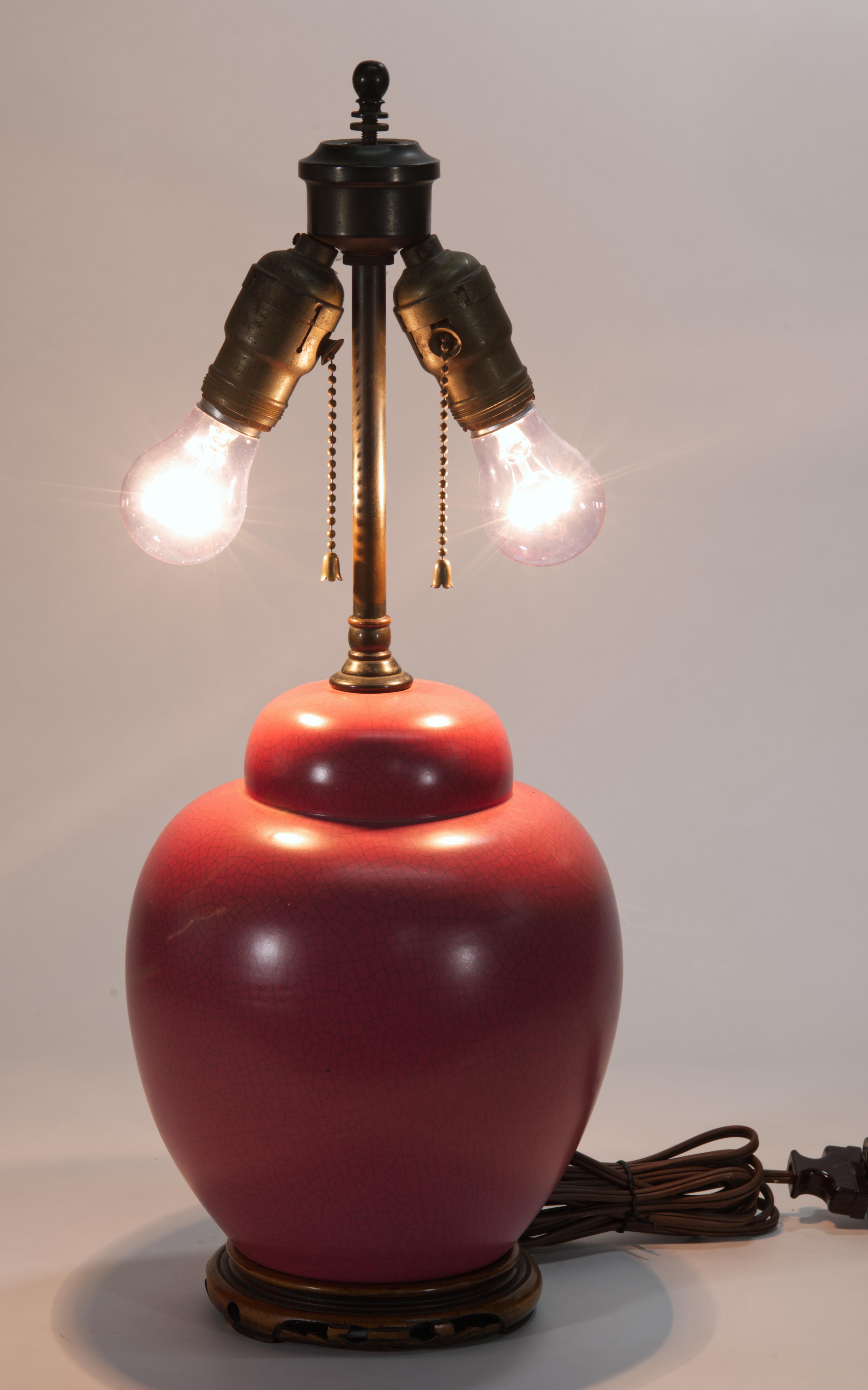  Vintage accent or table lamp features the classic ginger jar or urn shaped body mounted on carved wooden pedestal. The ceramic body of the lamp is decorated with unusual raspberry red glaze with elegant craquelure tratment, and is finished with the