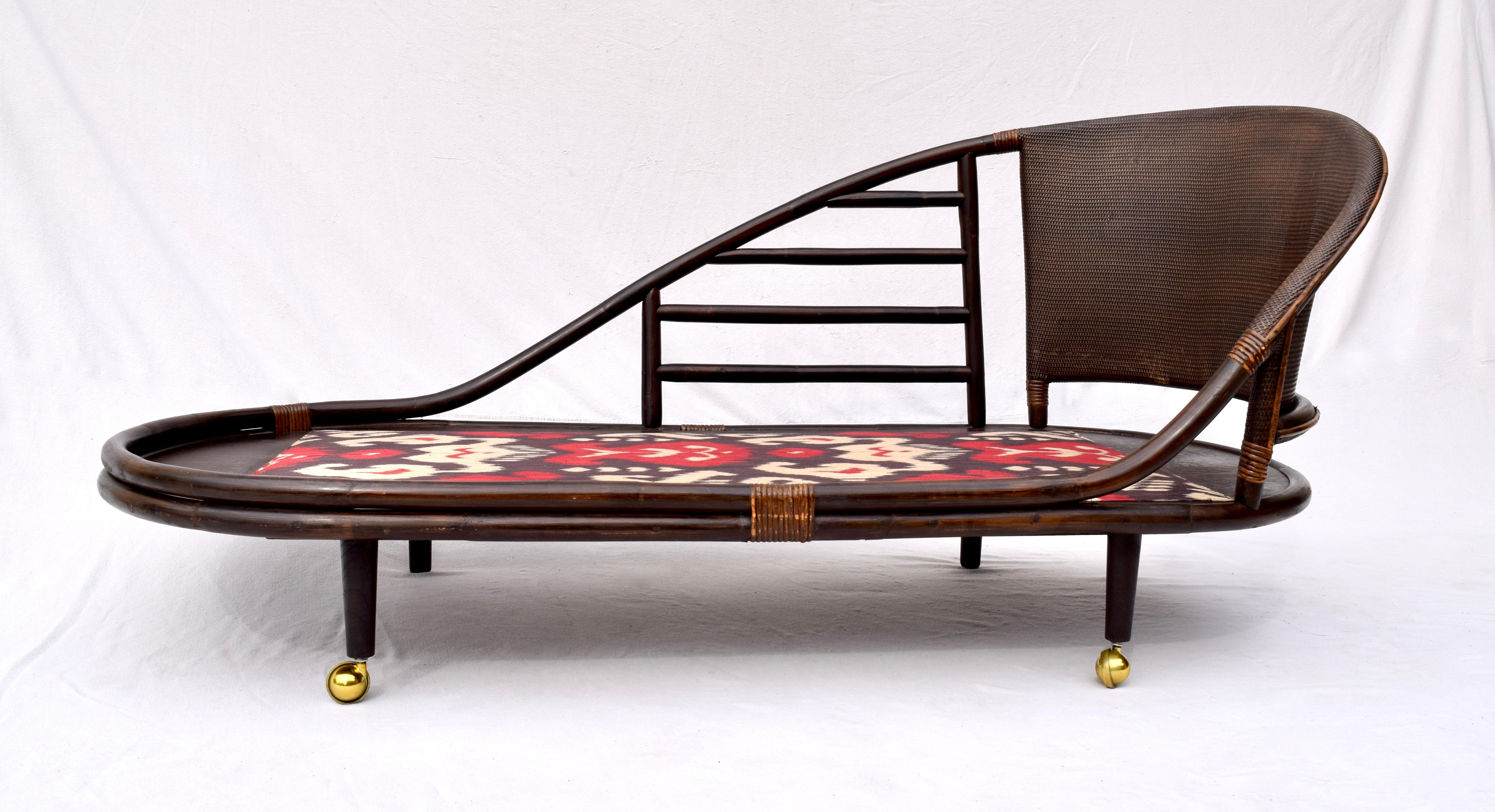 A sculptural chinoiserie rattan chaise lounge with curved saucer shaped grasscloth back rest.
Newly upholstered in striking Ikat silk this unusual chaise is cleverly designed with two brass casters allowing for easy lift and maneuvering from the