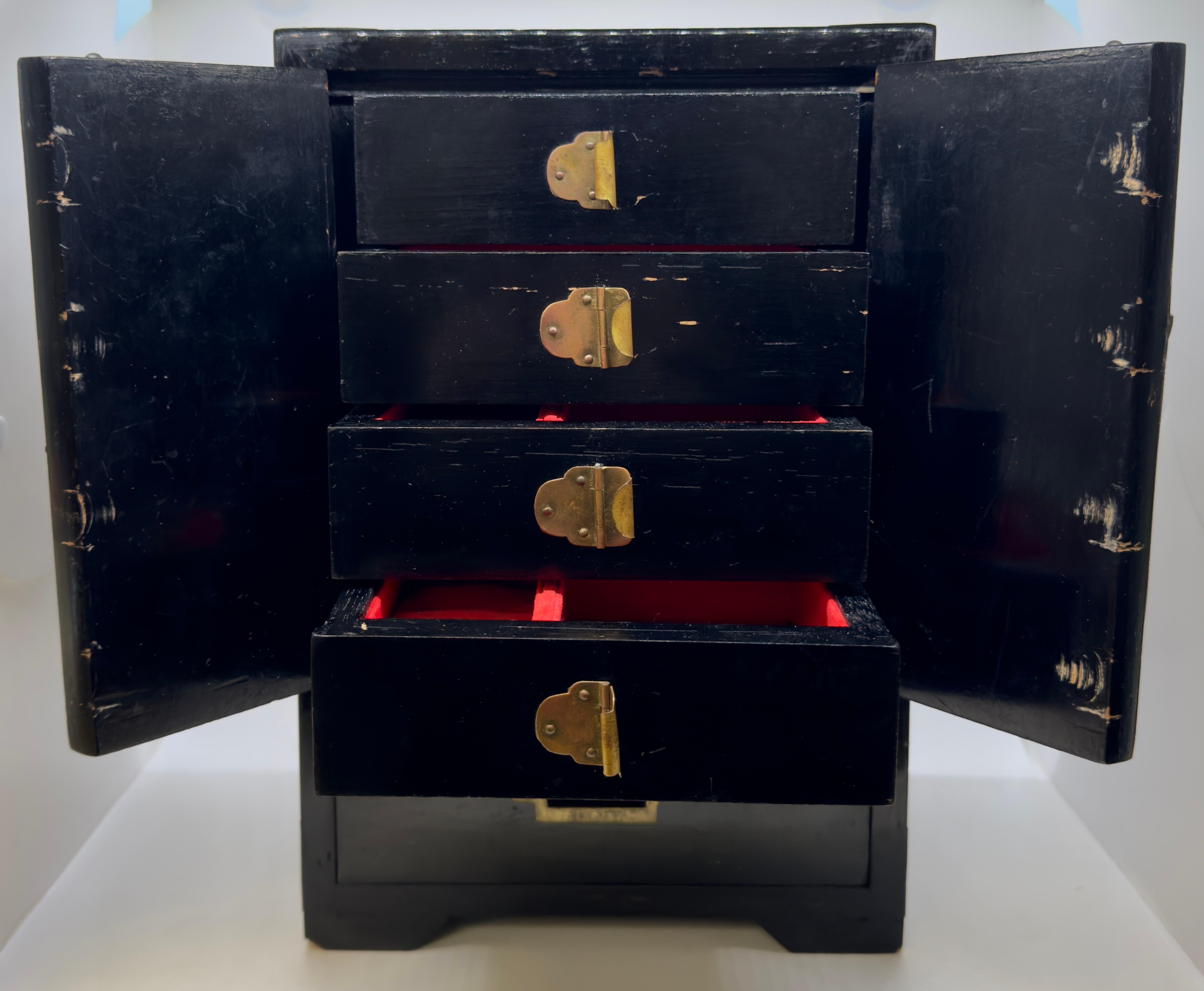 A Chinoiserie lacquered jewelry chest in striking black. The chest features two doors adorned with graceful women figures facing aha other. Upon opening these doors, a treasure trove awaits within—four small drawers delicately crafted to house your