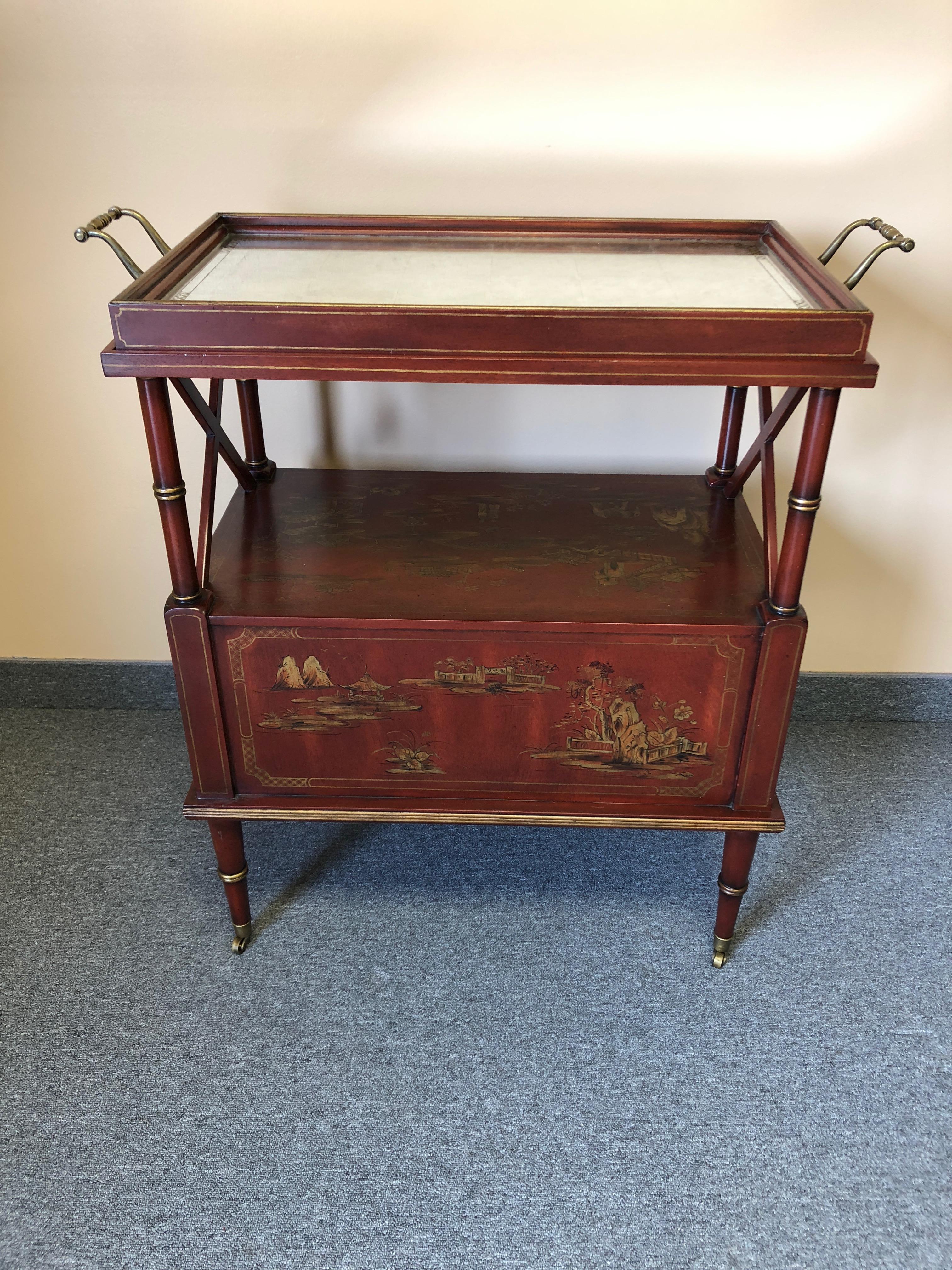 An elegant cinnabar red and gold chinoiserie decorated bar or serving cart having a removable tray that's aged mirror with black and gold painted decoration. The body of the cart has Asian landscapes, figures and animals, and is finished front, side