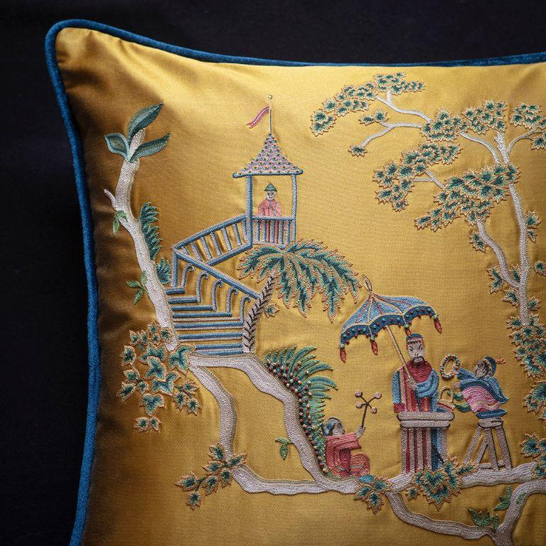 Le coussin brodé Cathay de Beaumont & Fletcher s'inspire du style Chinoiserie, très populaire en France au XVIIIe siècle. Fabriqué entièrement à la main, il présente un recto en satin doré et un verso et un passepoil en velours de soie contrastant