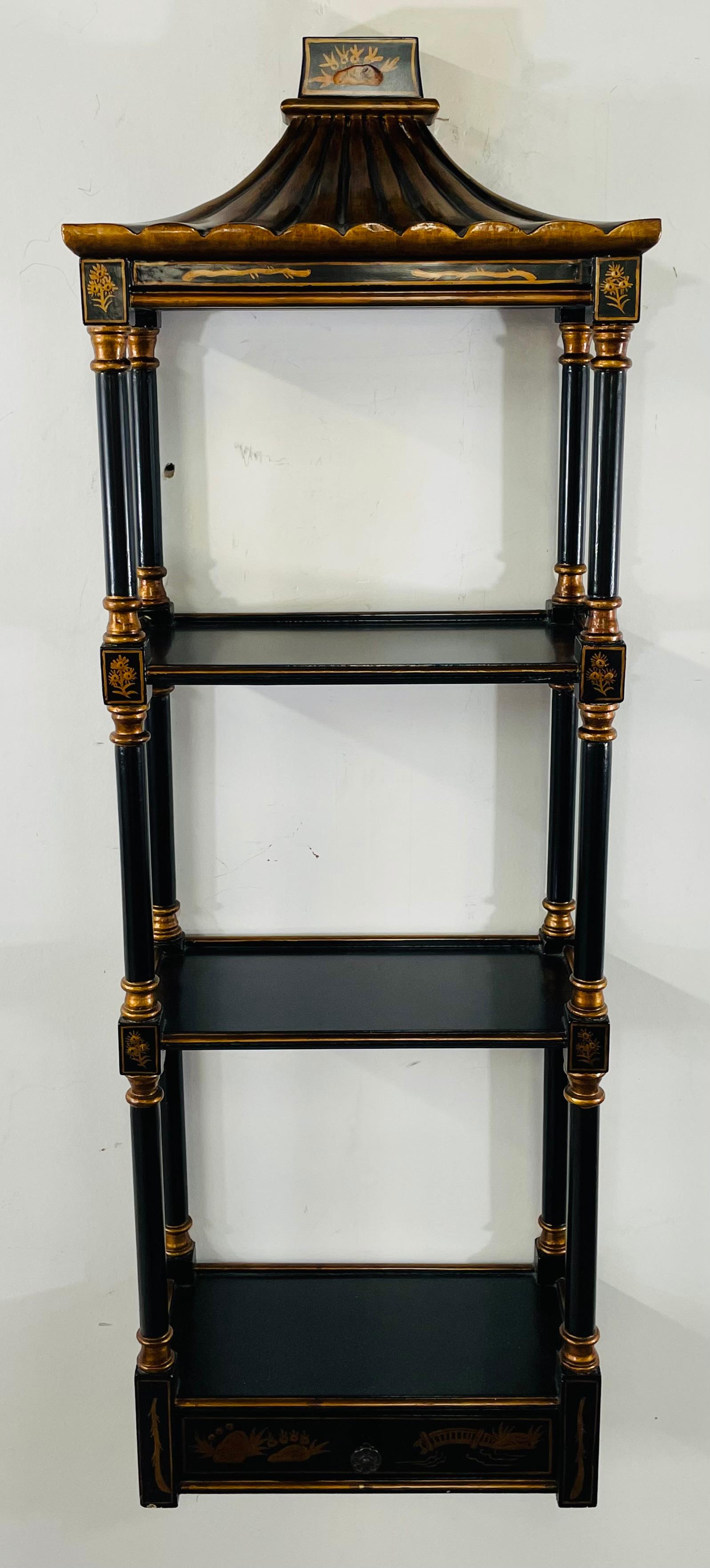 A late 20th century Chinoiserie style lacquered black wood with gilt highlight wall rack . The wall rack has three shelves and features a Pagoda form and a faux-bamboo design with a lower drawer. 

Dimensions: 12.75
