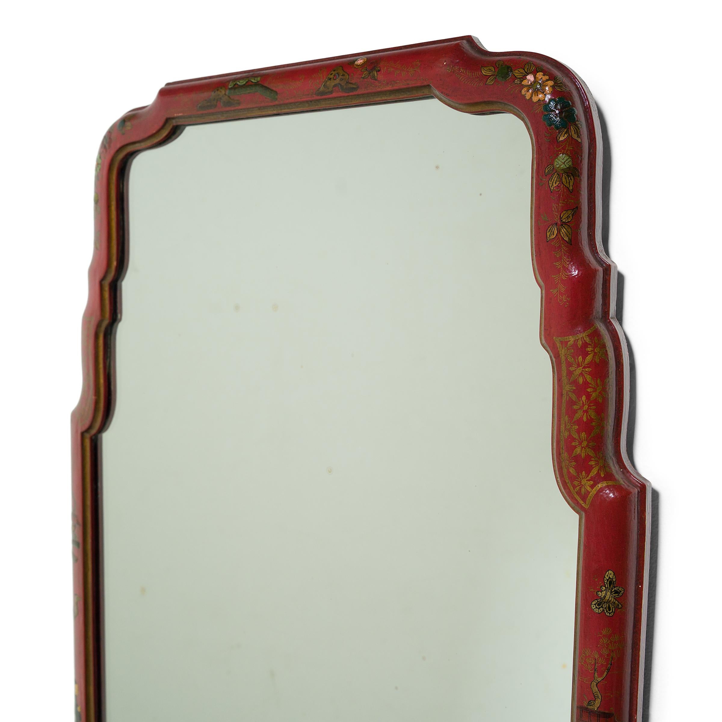 This vintage wall mirror has an elongated form, with a rectangular base and arched top shaped by sinuous, stepped corners. The mirror is decorated in the chinoiserie style, painted with robed figures, floral motifs, and auspicious objects atop a red