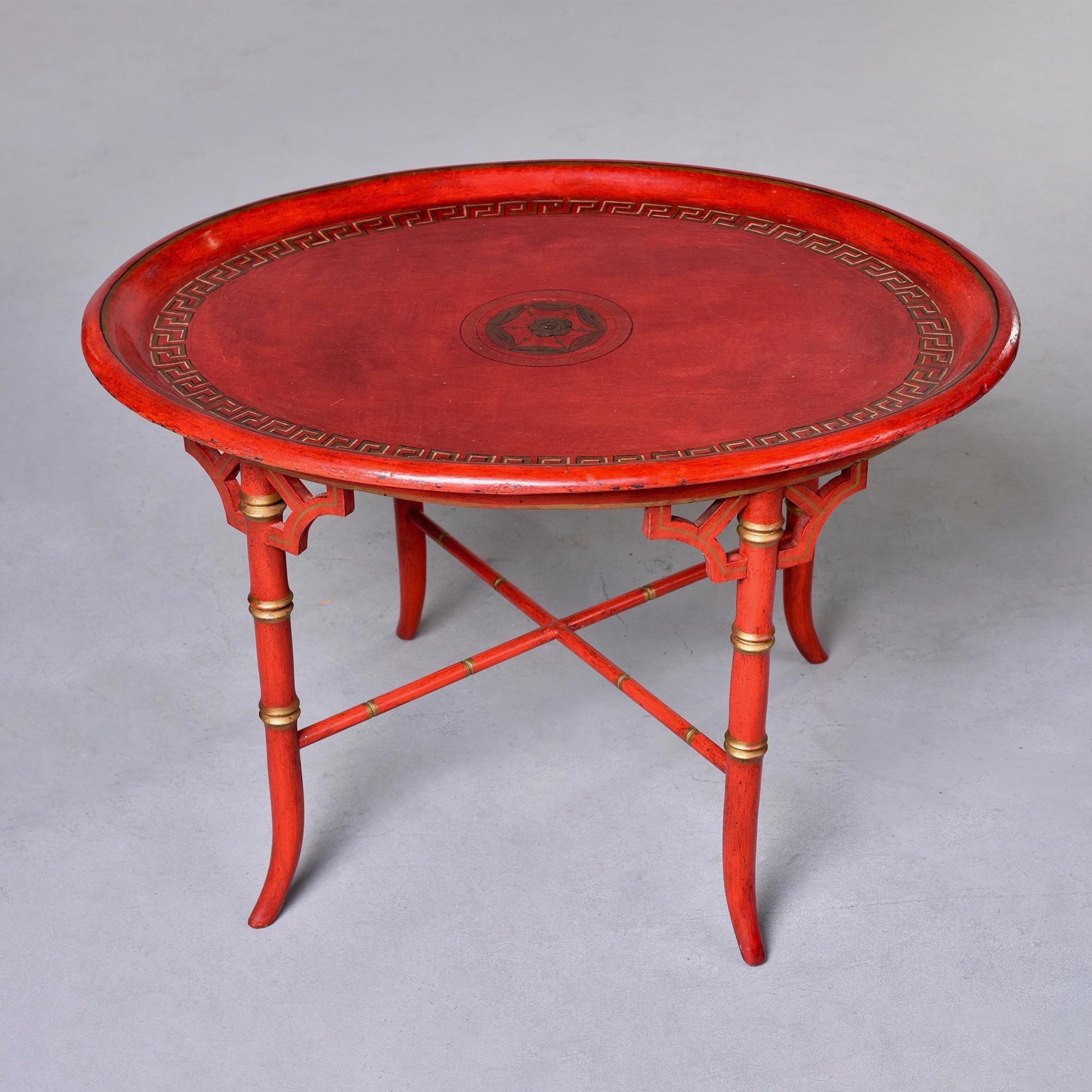 Found in England, this circa 1930s red round Chinoiserie style side table features a faux bamboo base with X-form stretcher and gilded details. Round table top is has a decorative Greek key painted gilt border on inside edge and decorative painted