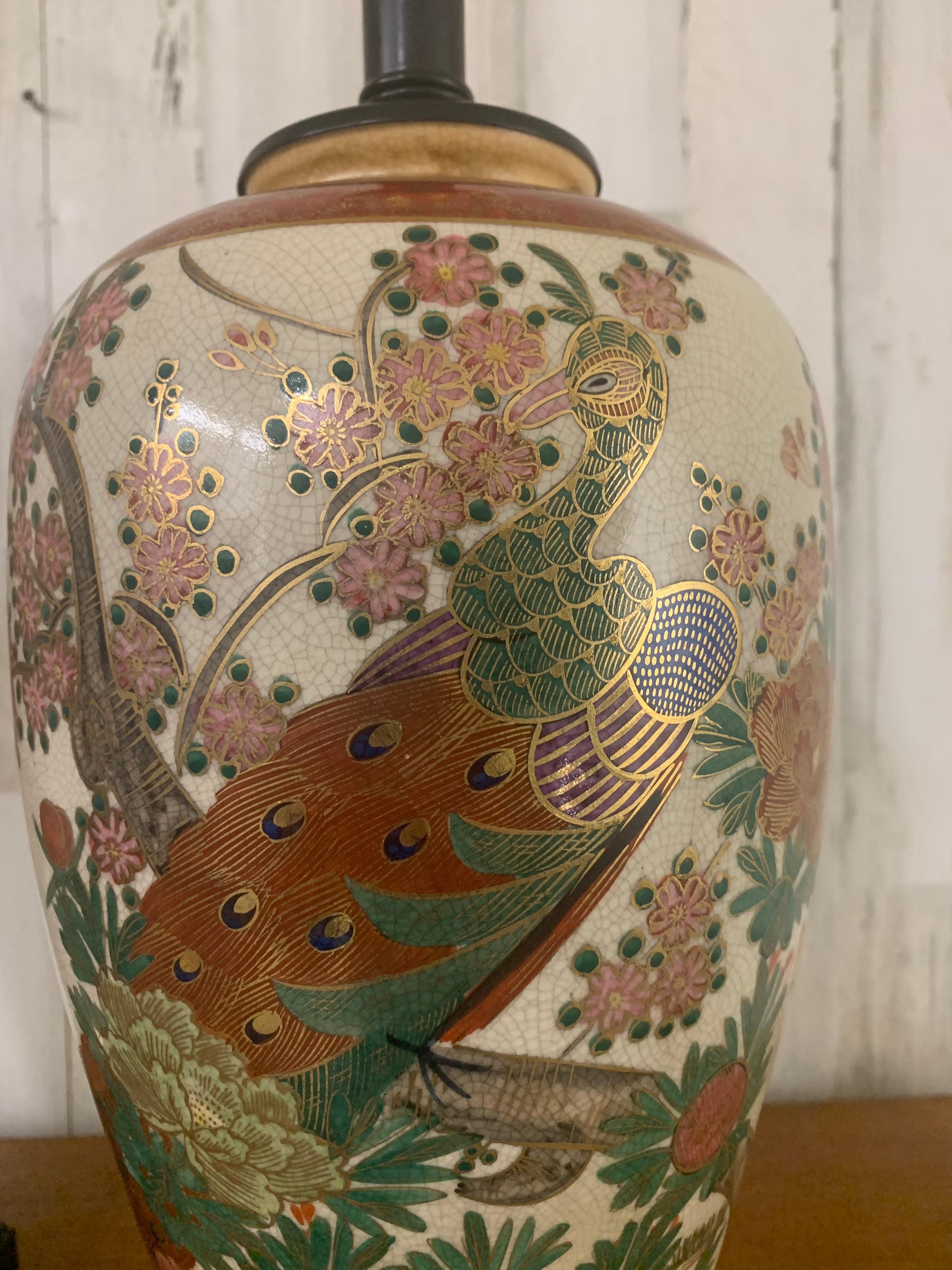 Beautiful pair of ceramic table lamps painted peacocks and cherry blossom trees a gold design back ground mounted on ebonized wood bases.    23