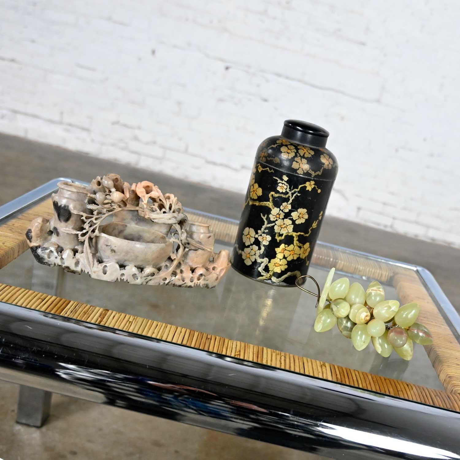 Lovely chinoiserie vignette including a soap stone carving, a black tin tea canister comprised of hand painted gold floral detail, a lid, and a bunch of light jade colored stone decorative grapes. Beautiful condition, keeping in mind that these are