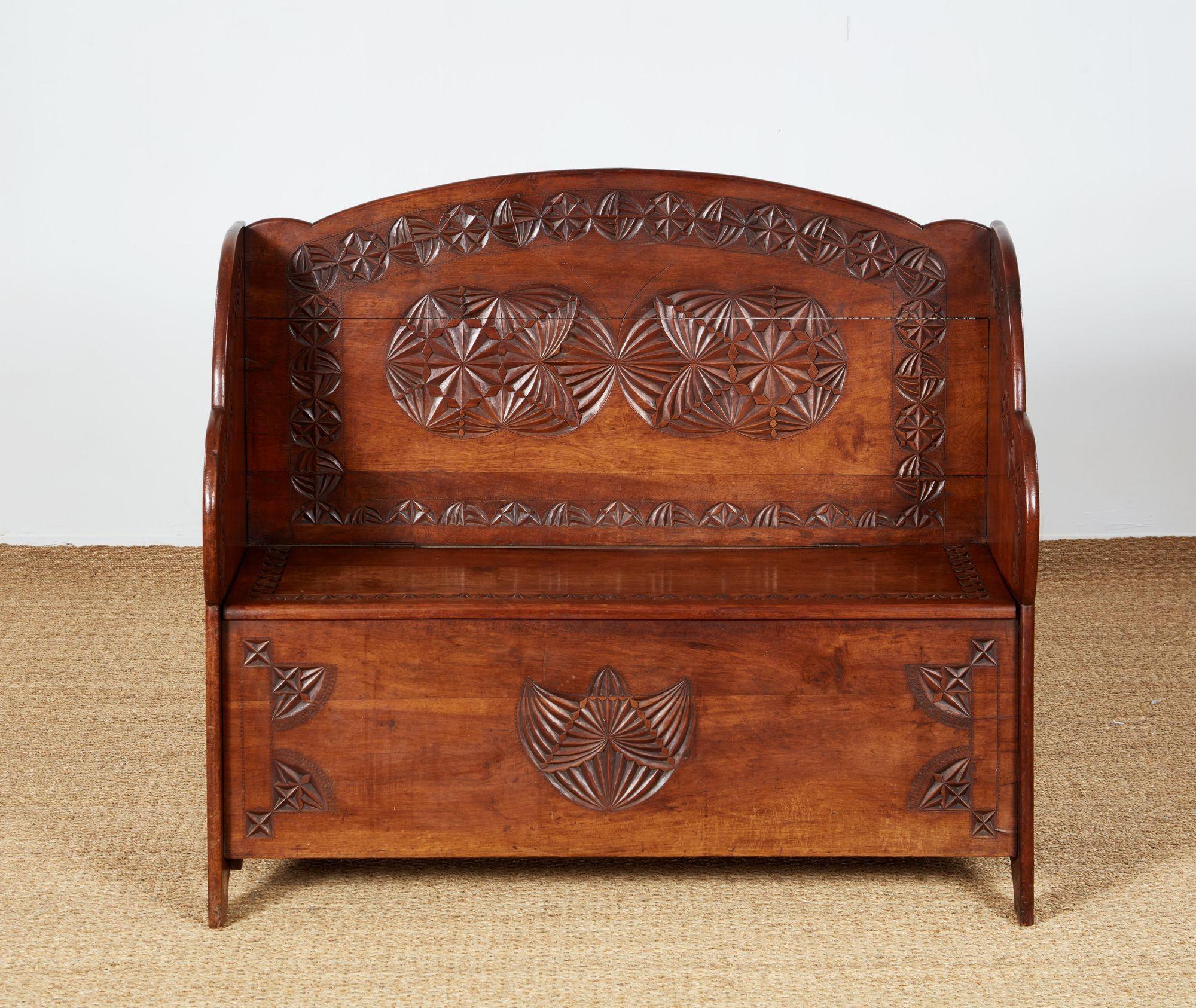 A settle bench with solid arched back and shaped wings, having lift top bench seat revealing storage. Geometric chip carved decoration to back, sides and front. Good color and useful size for a hall bench or mudroom seat.