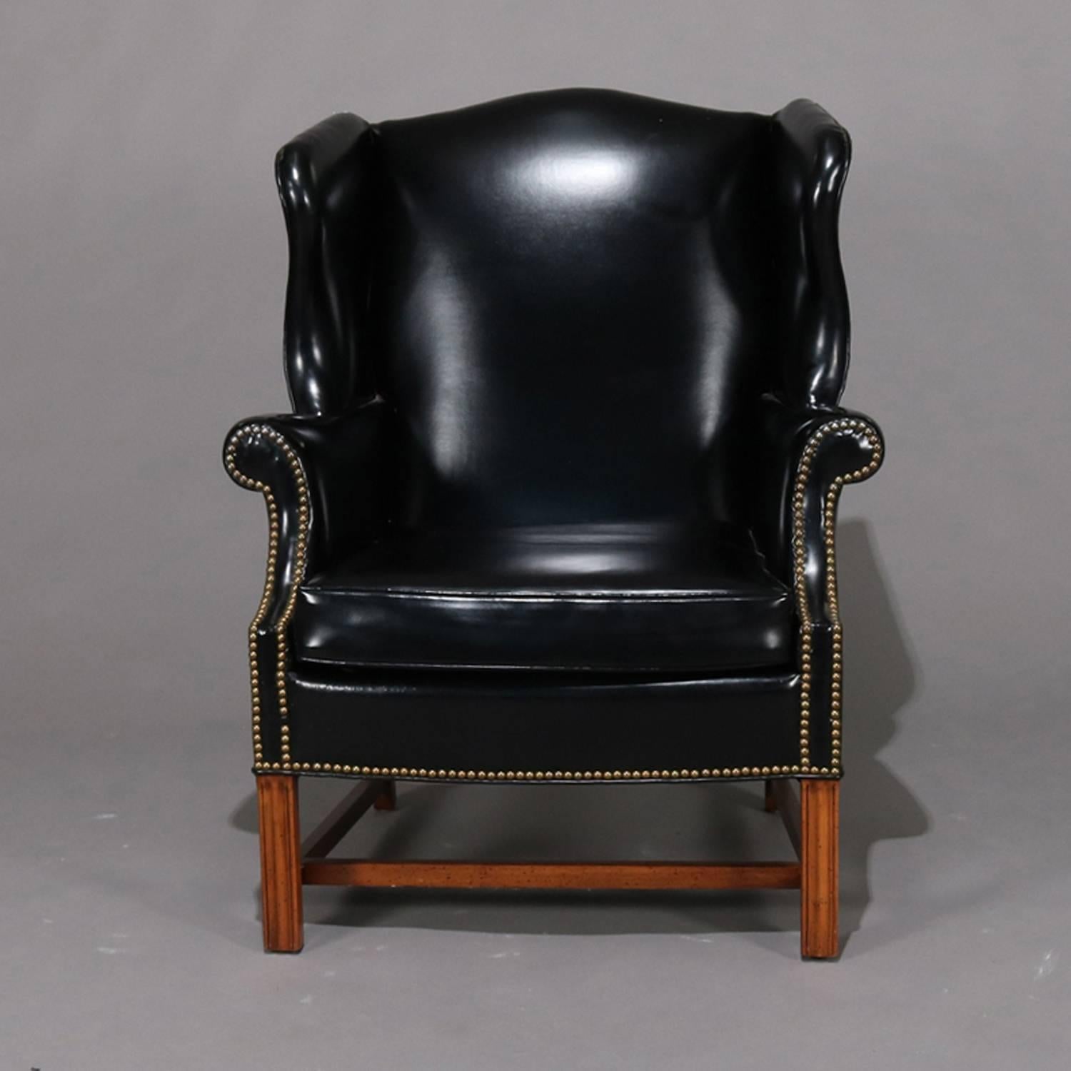 Chippendale style fireside wing back armchair features scalloped wings and scrolled arms with black faux leather upholstery and brass tacks, partial original label, 20th century.

Measures: 40